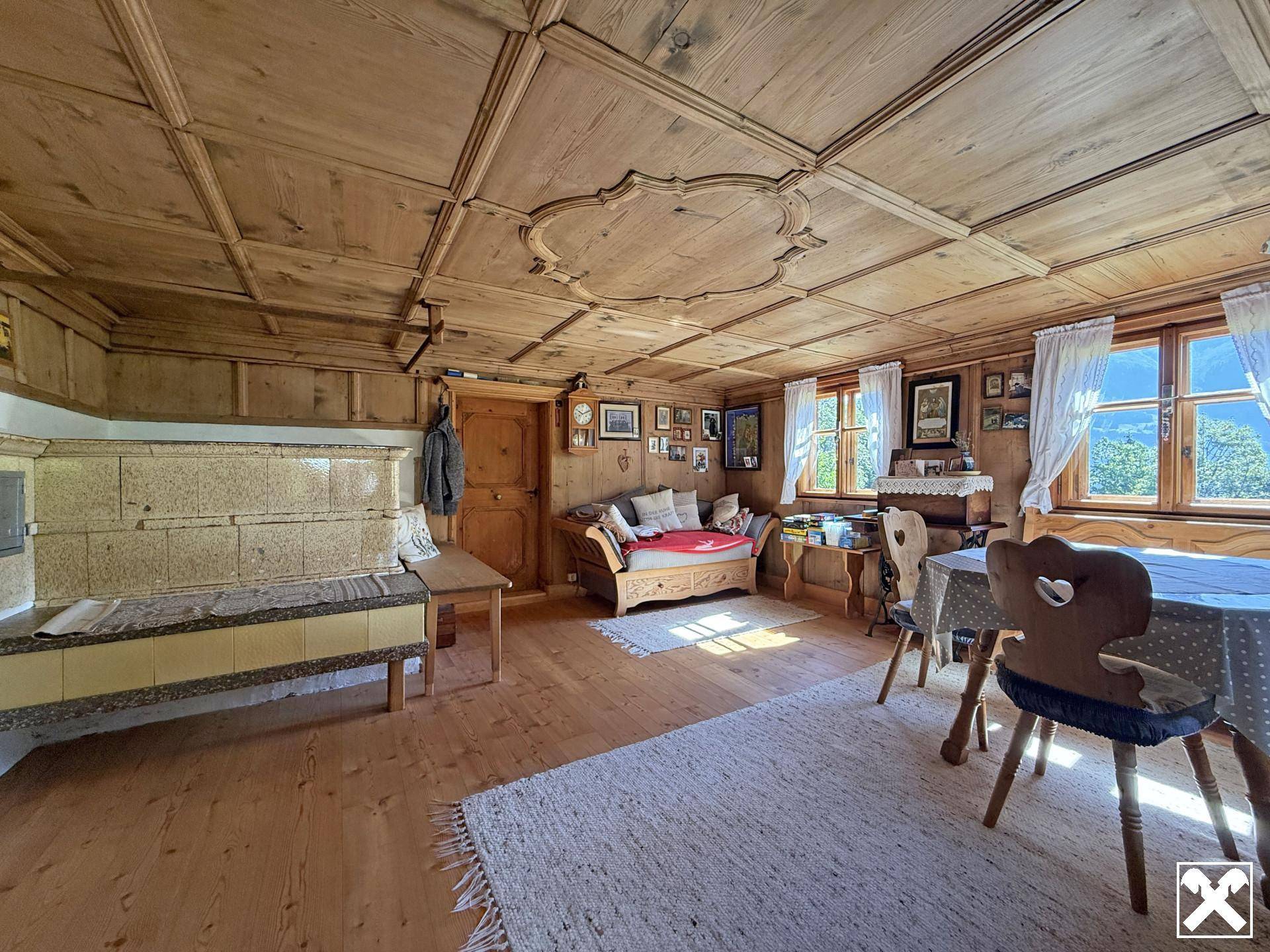 Geräumiger Wohnbereich mit Holztäfelung, Kassettendecke, Kachelofen und Blick auf die Berge.