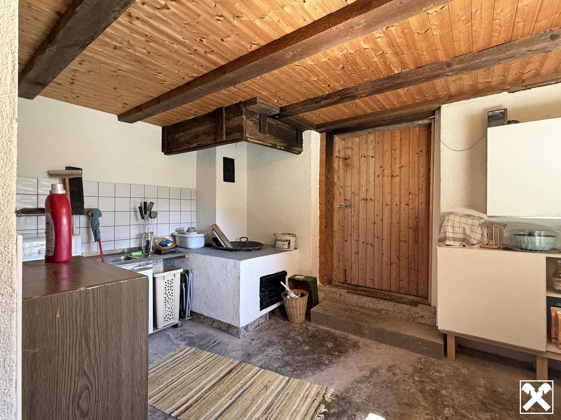 Einfache Küche mit gefliestem Bereich, Holzdecke und einem traditionellen Holzofen.