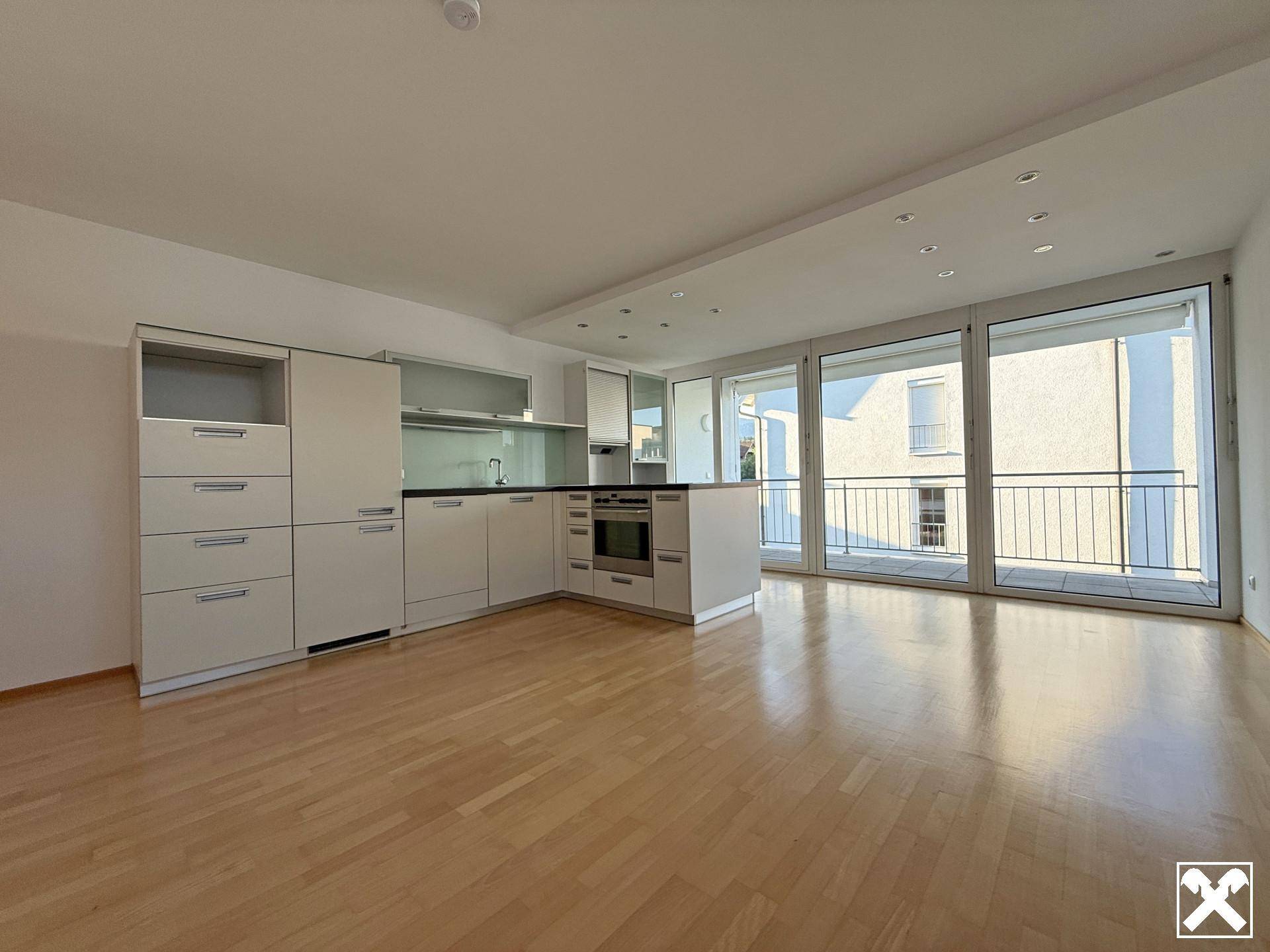 Helles, offenes Wohnzimmer mit integrierter Küche, Parkettboden und Zugang zum Balkon.
