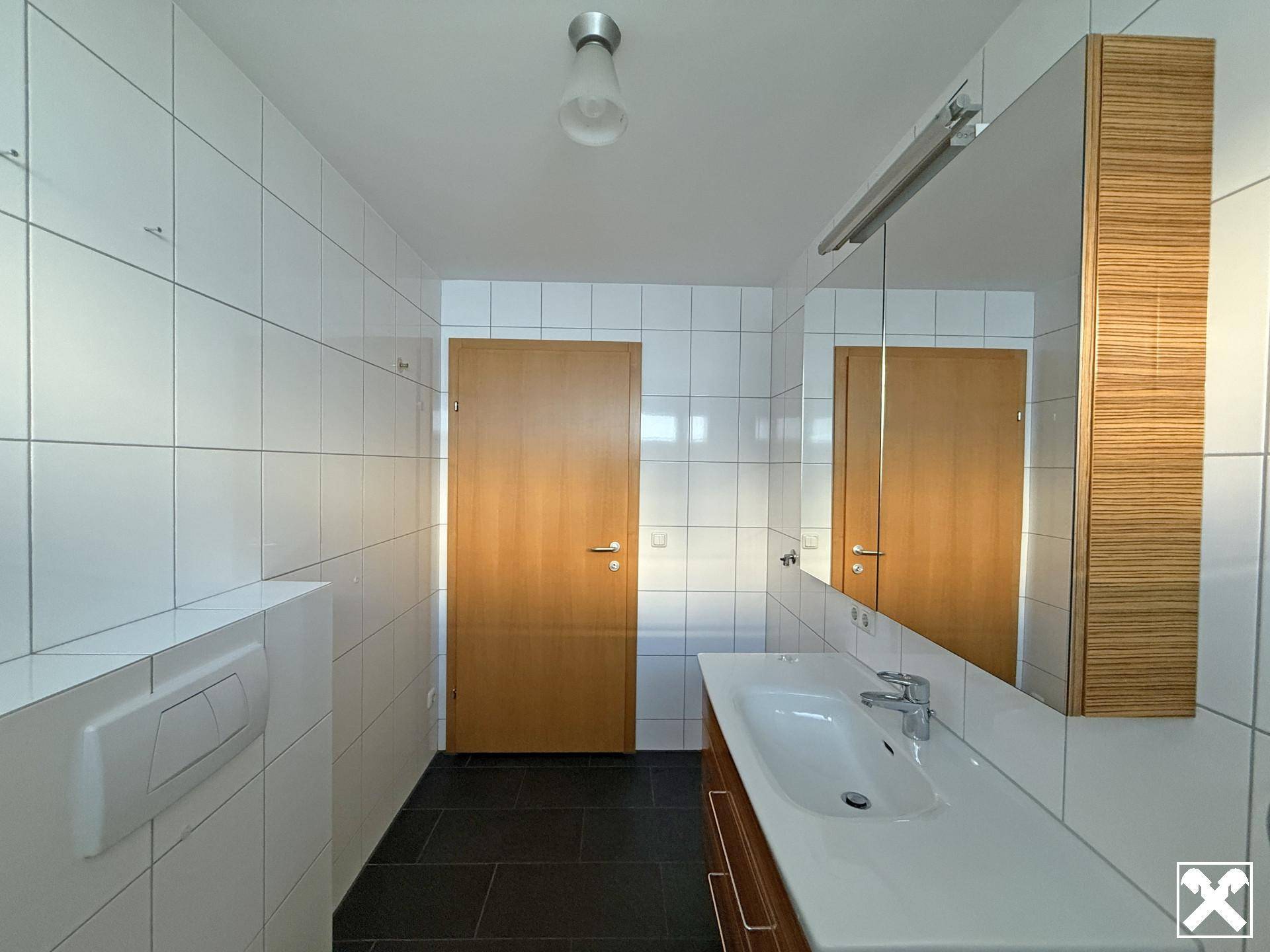 Helles Badezimmer mit großem Waschbecken, Spiegelschrank und dunklem Fliesenboden.