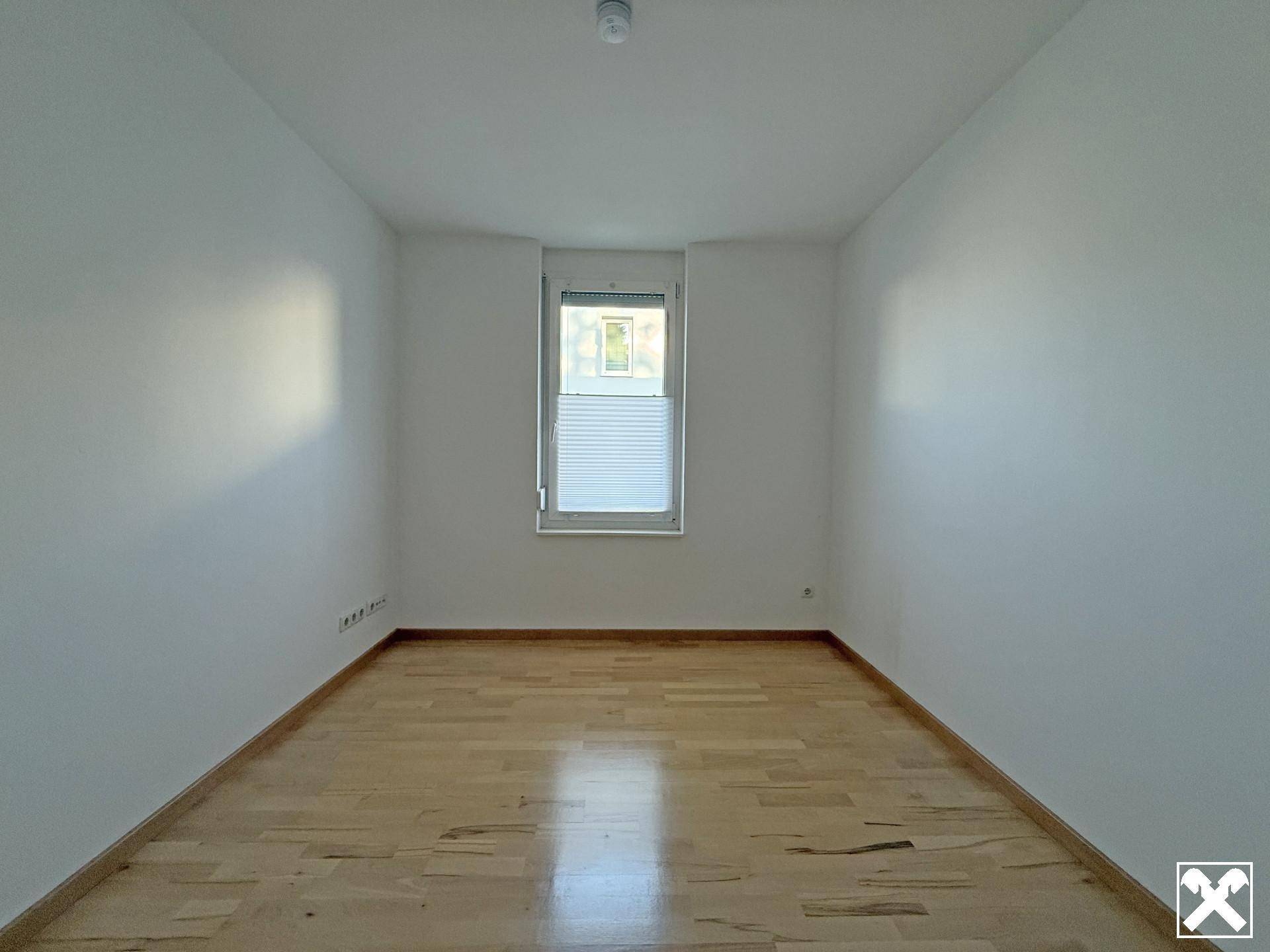 Heller, leerer Raum mit Parkettboden und einem Fenster, das Tageslicht hereinlässt.