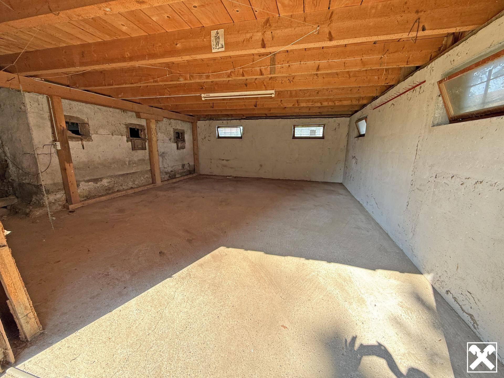 Heller Kellerraum mit Betonboden, rauen Wänden und sichtbaren Holzdeckenbalken, ideal als Lagerraum.