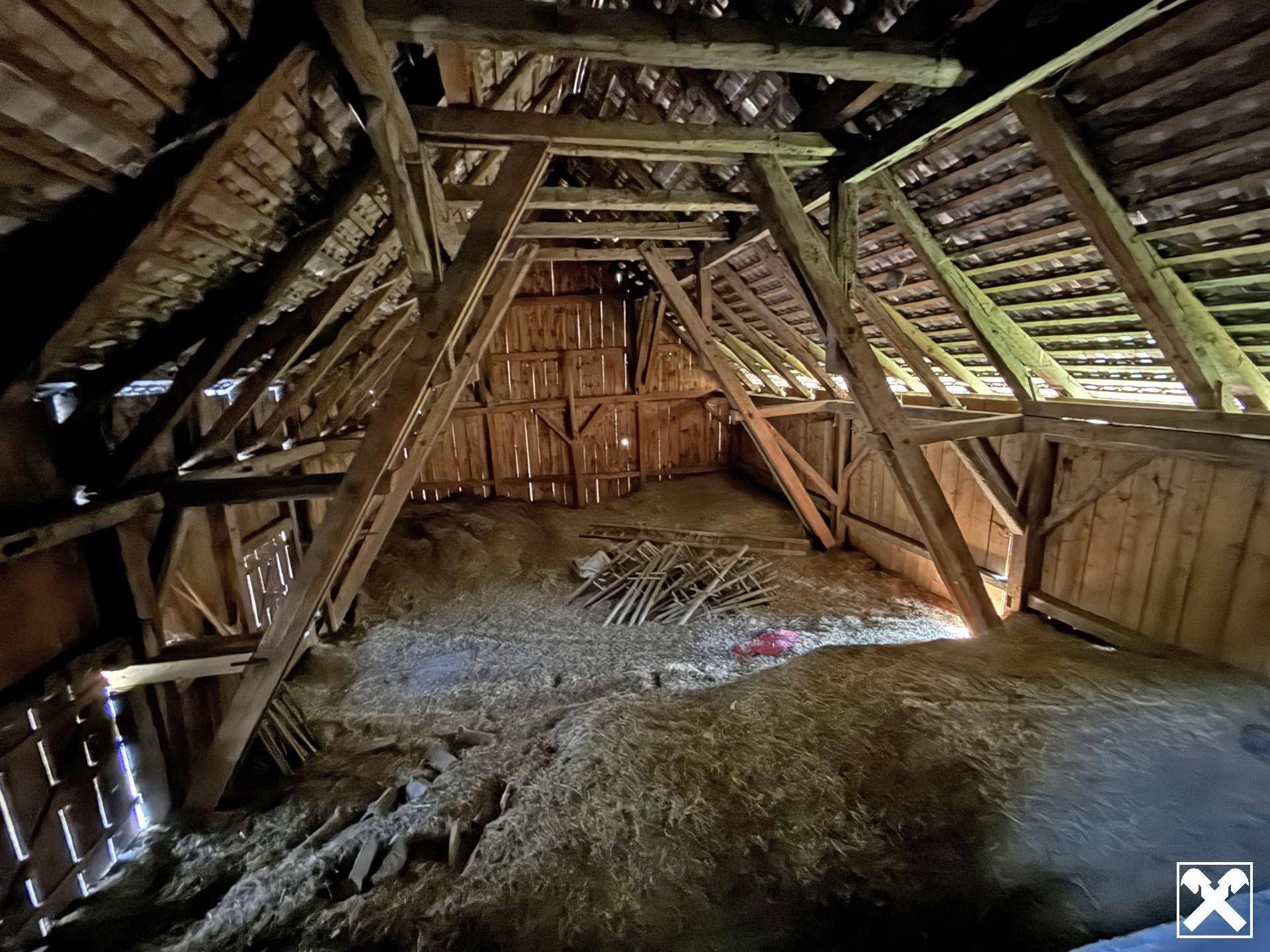 Geräumiger Dachboden oder Scheunenbereich mit sichtbaren Holzbalken und Heu auf dem Boden.