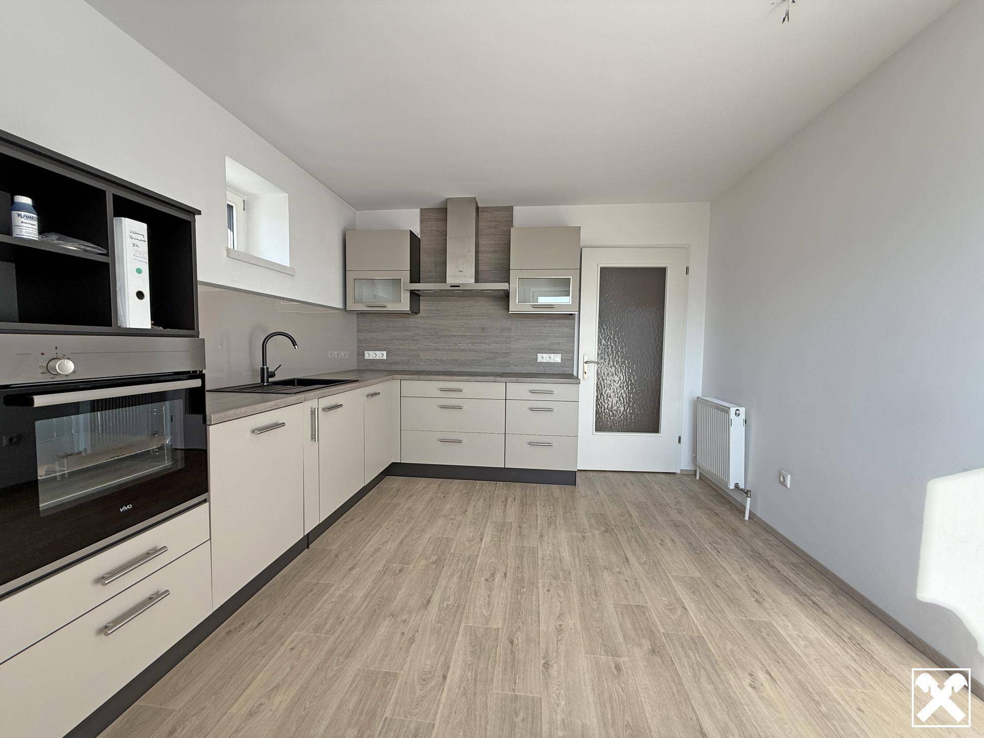 Moderne Einbauküche in hellen Farbtönen mit integrierten Geräten und Laminatboden.