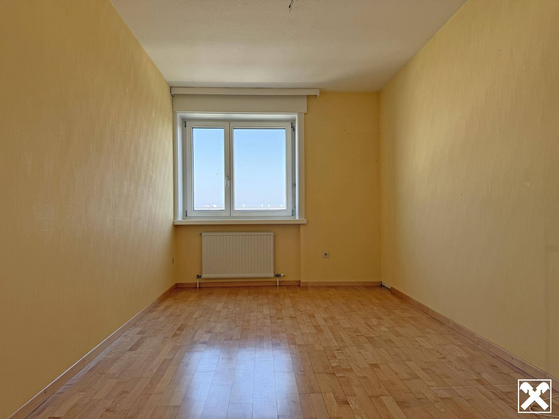 Geräumiges Zimmer mit Parkettboden, gelben Wänden und einem großen Fenster für viel Licht.
