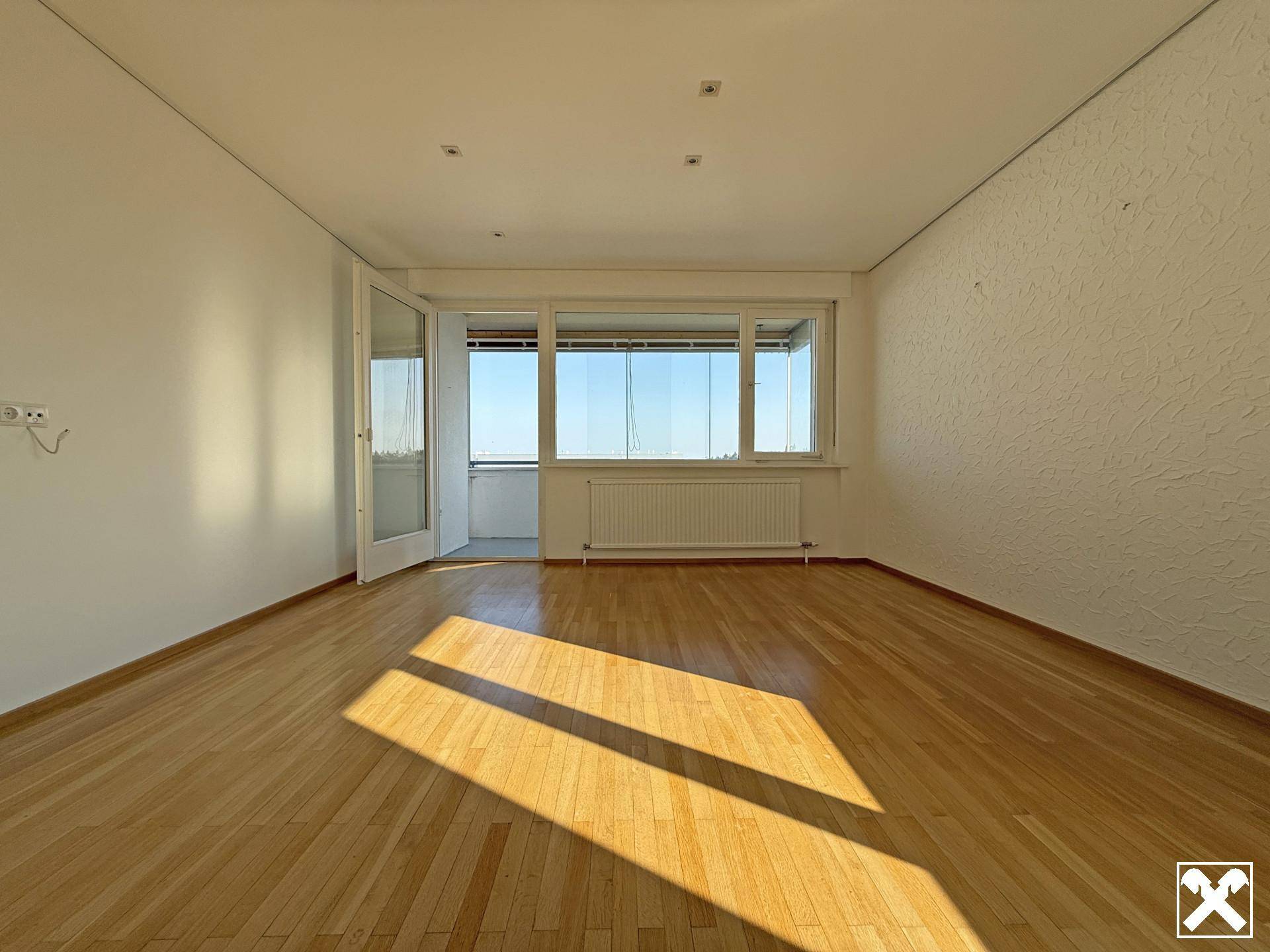 Helles Wohnzimmer mit Parkettboden und direktem Zugang zu einem verglasten Balkon.