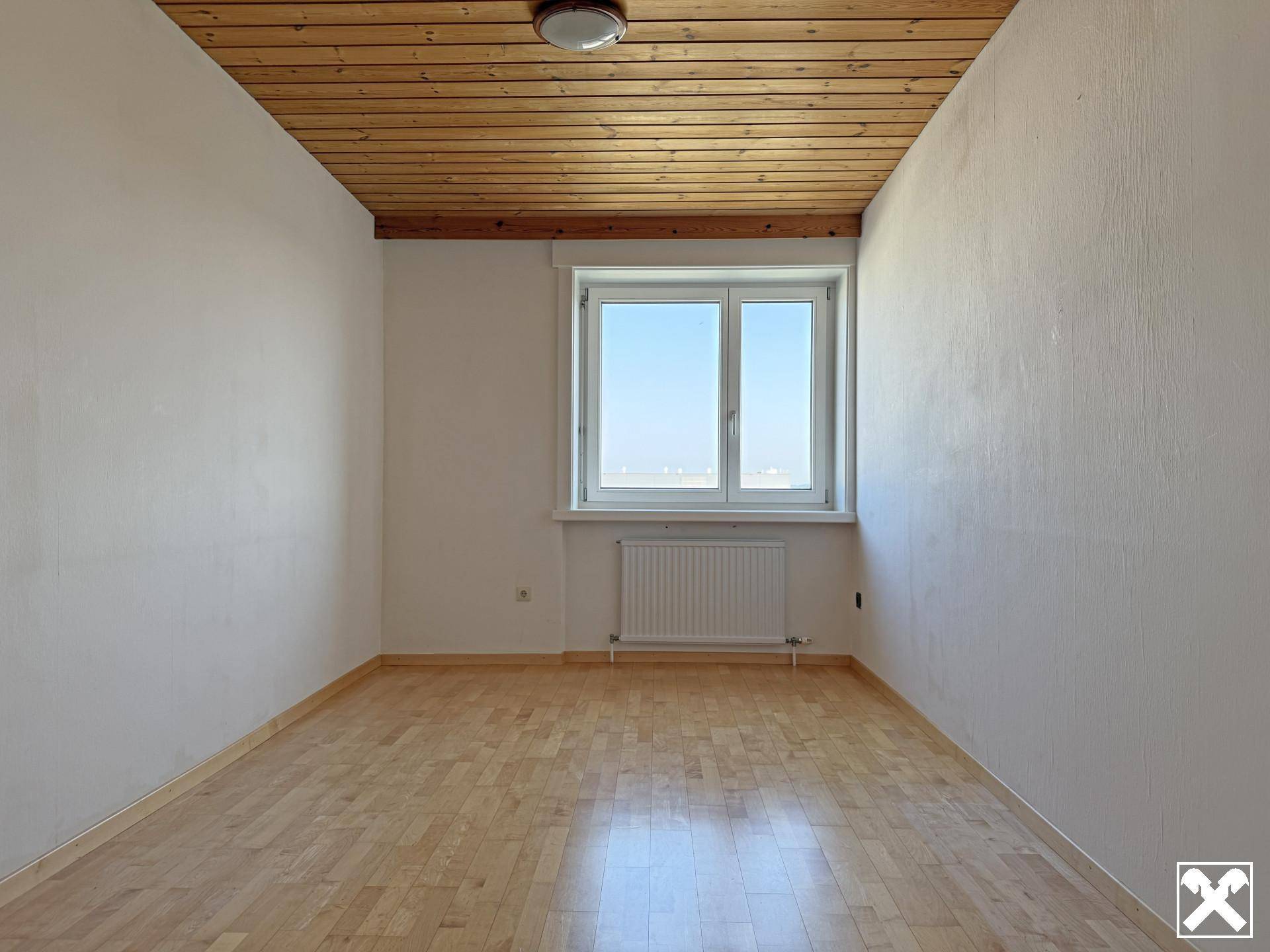 Helles Zimmer mit Holzbalkendecke, Parkettboden und weiß gestrichenen Wänden.