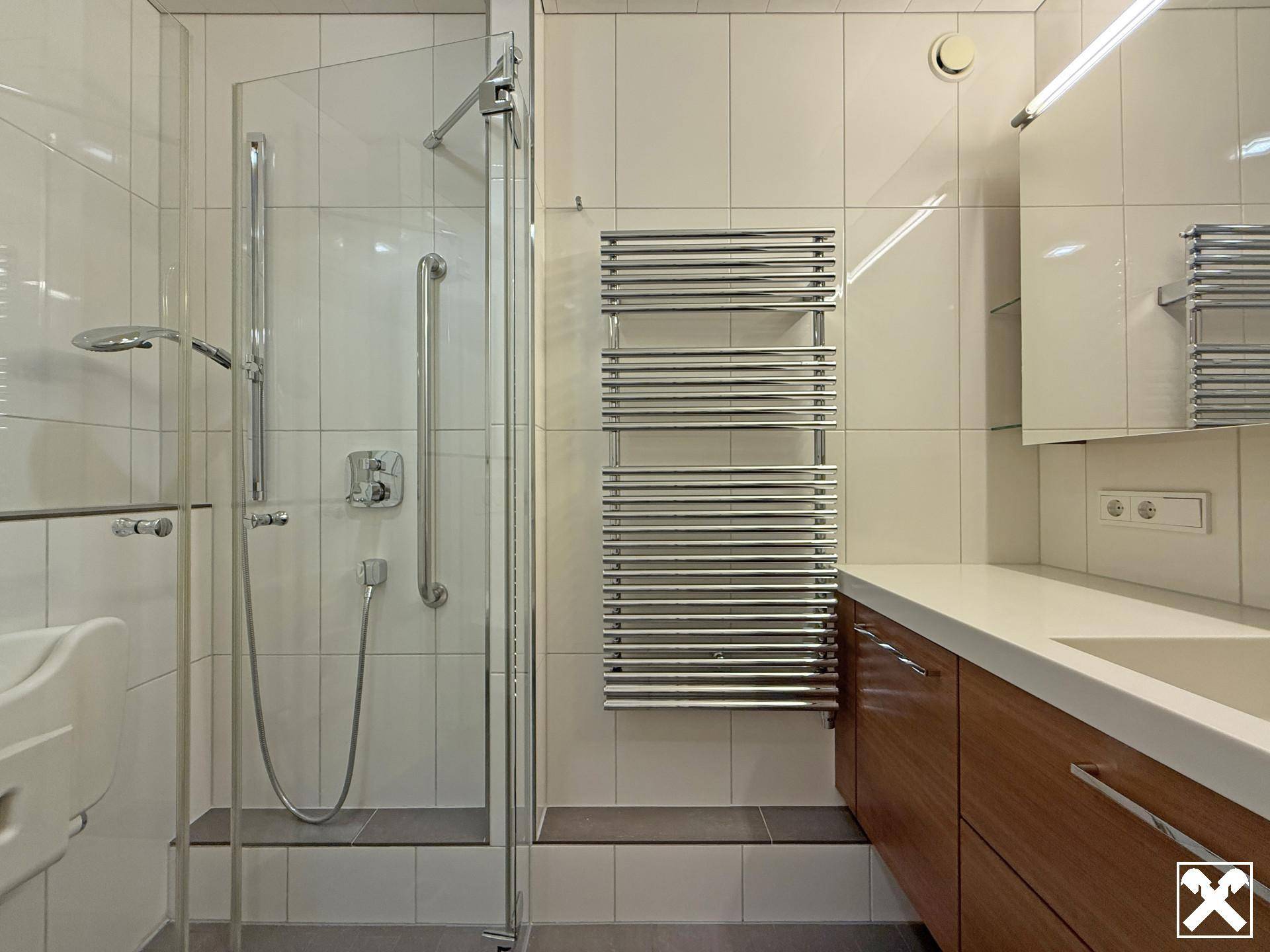 Modernes Badezimmer mit ebenerdiger Dusche, Handtuchheizkörper und Waschtisch mit Holzunterschrank.