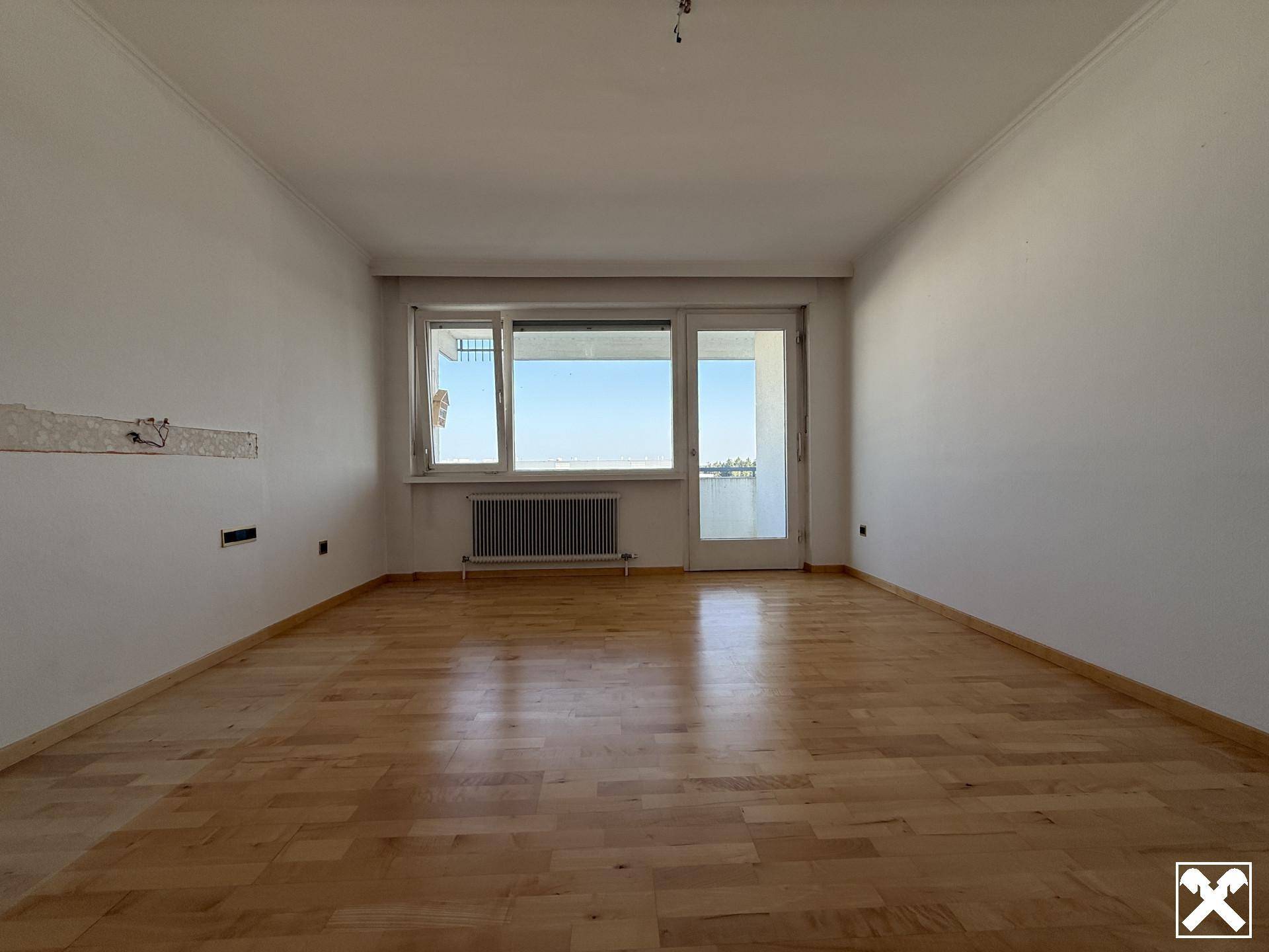 Heller, leerer Wohnraum mit Holzboden und Zugang zu einem Balkon oder einer Terrasse.