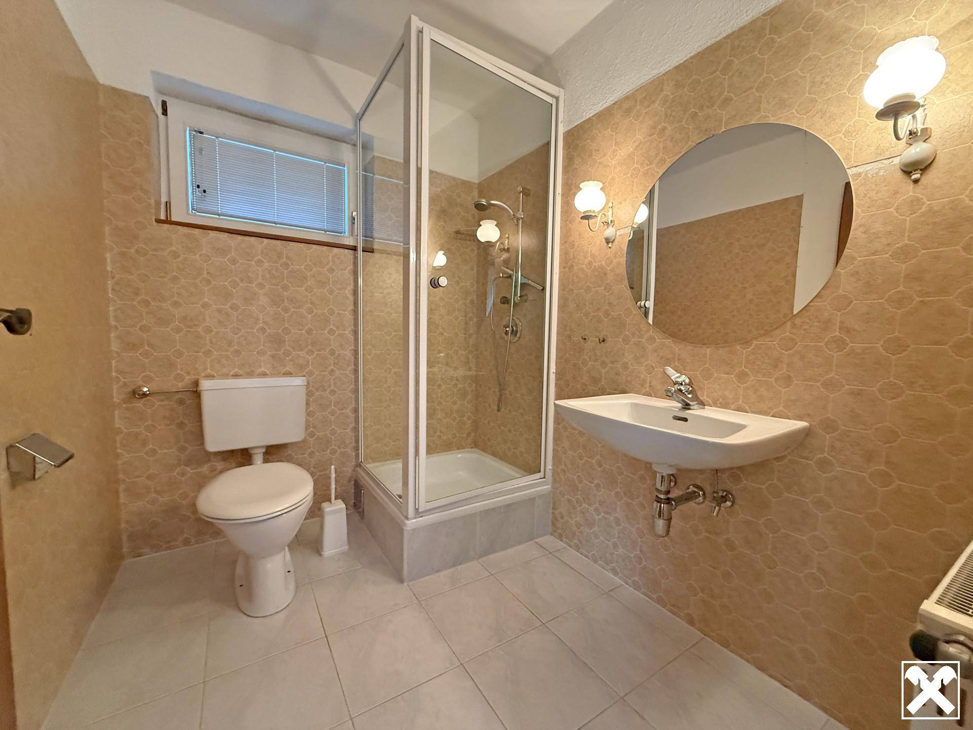 Badezimmer mit Duschkabine, WC und Waschbecken, ausgestattet mit beigen Fliesen und Fenster.