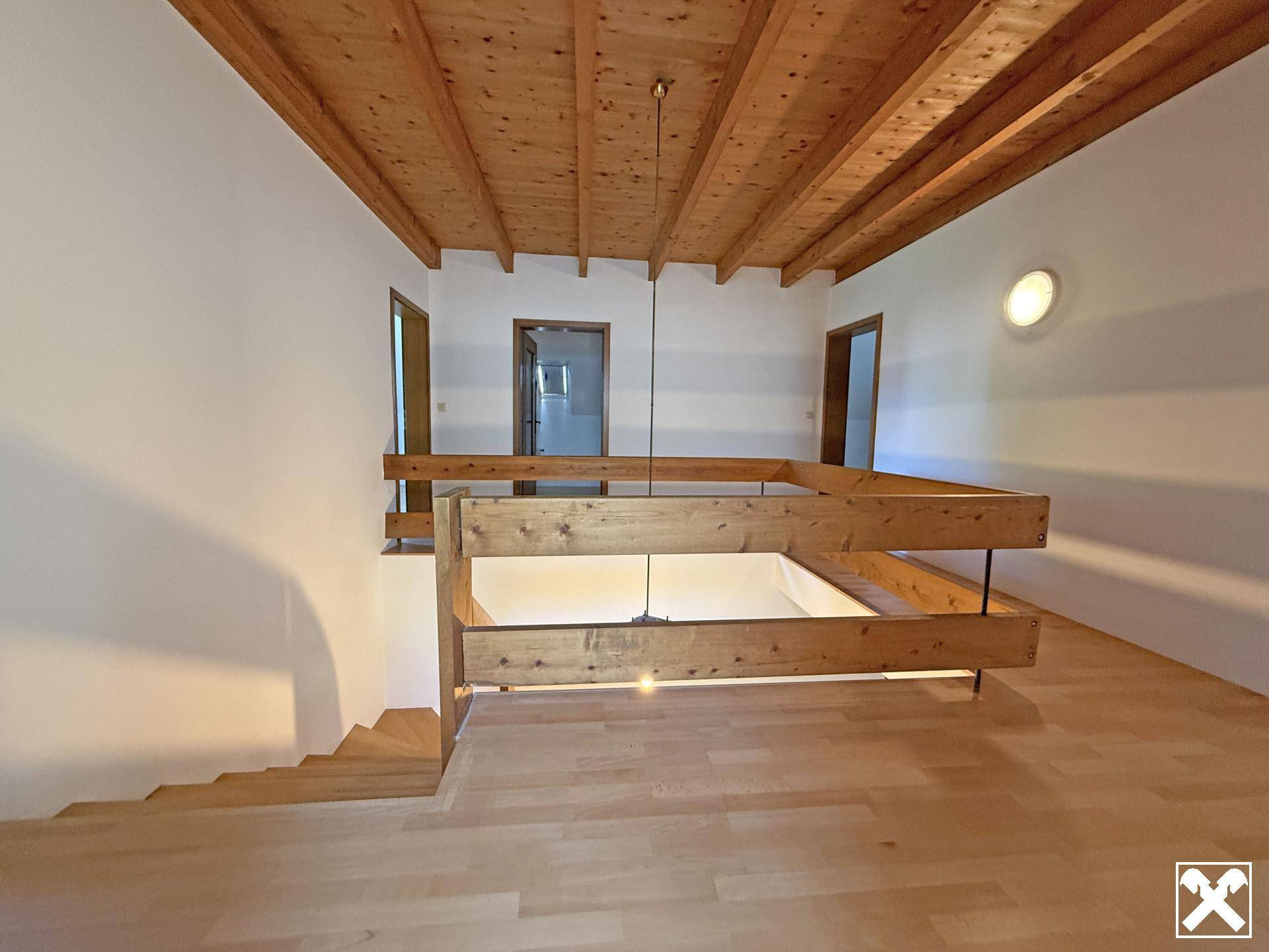 Offener Flurbereich im Obergeschoss mit Holzbalkendecke und Holzgeländer, das den Treppenbereich umgibt.