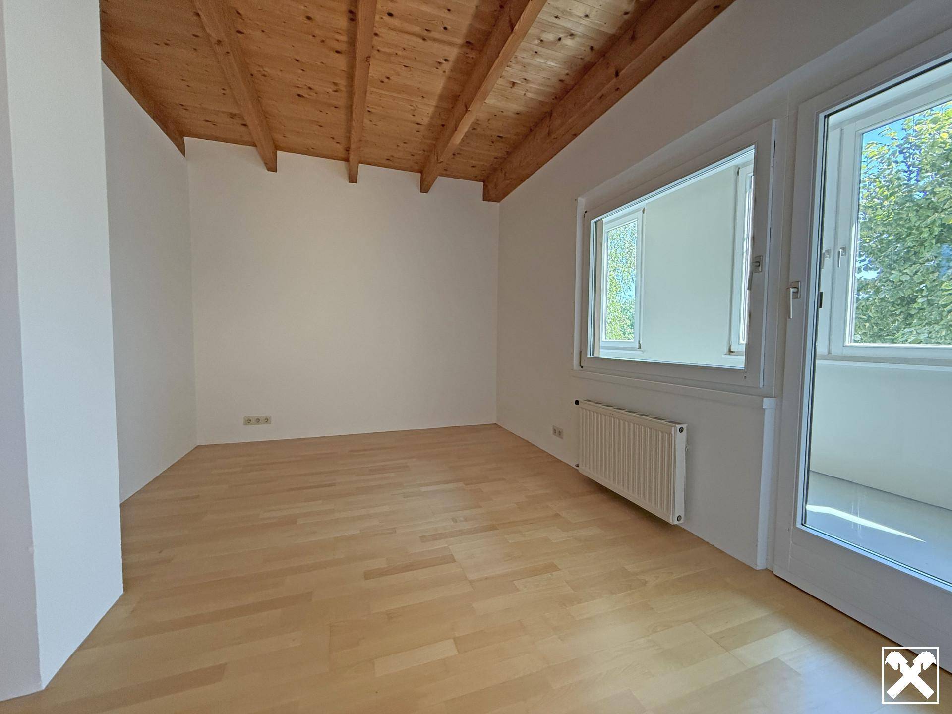 Schlafzimmer mit Holzbalkendecke, Parkettboden und Zugang zu einem Balkon, der viel Licht bietet.