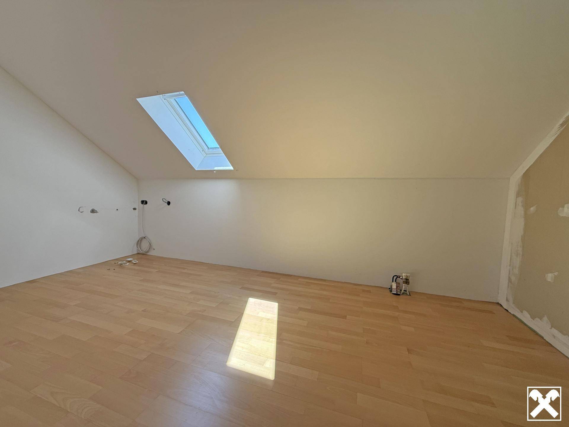 Helles Schlafzimmer im Dachgeschoss mit schräger Decke, Parkettboden und einem Dachfenster.