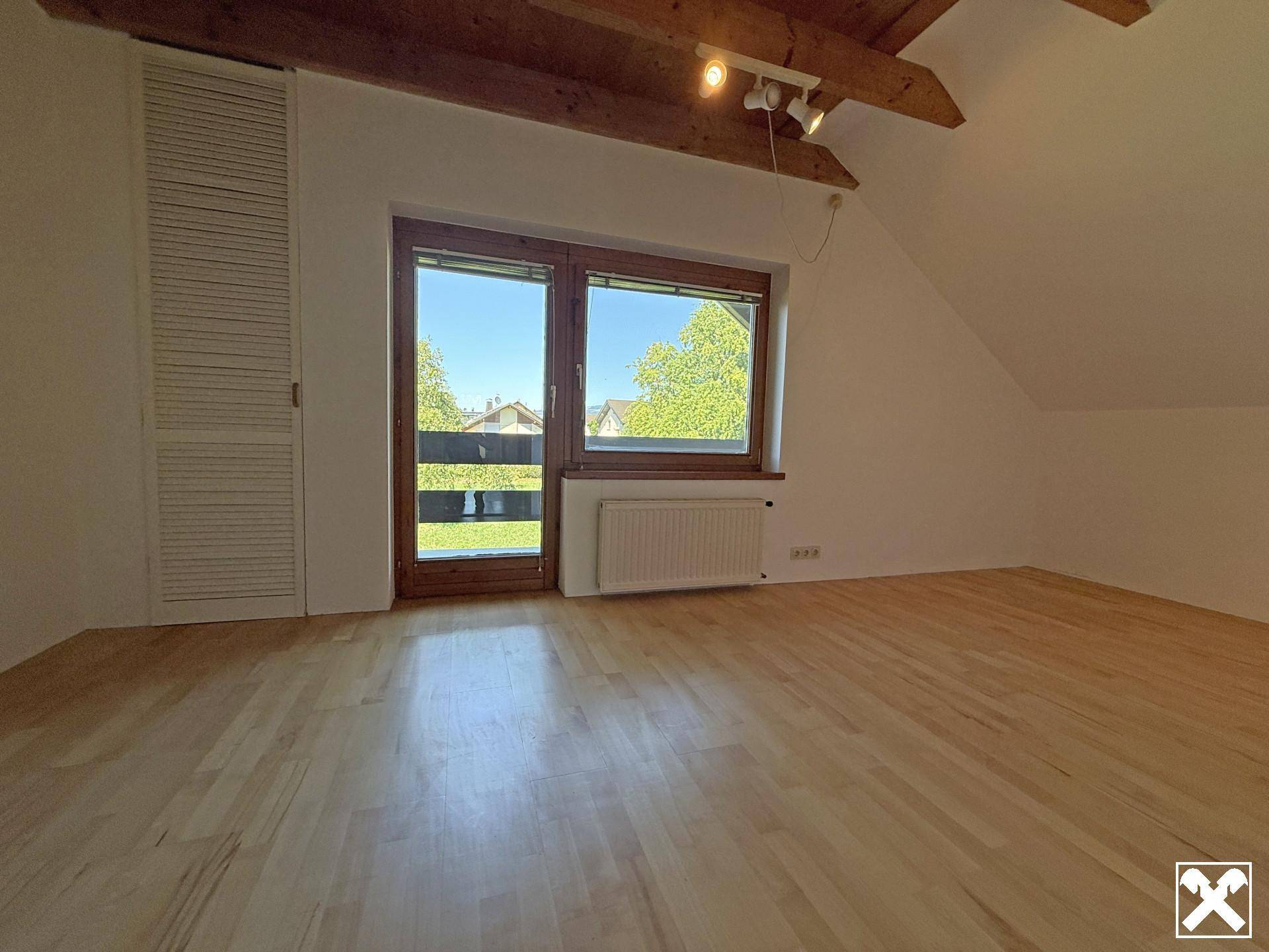 Gemütliches Schlafzimmer im Dachgeschoss mit Holzbalkendecke, Parkettboden und Fenster mit Ausblick.