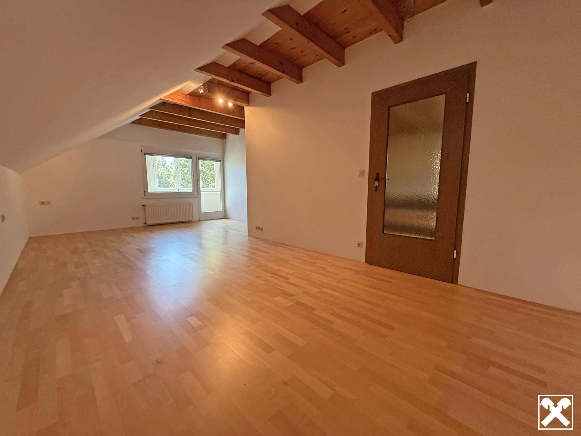 Helles Schlafzimmer im Dachgeschoss mit Holzbalkendecke, Parkettboden und Zugang zum Balkon.