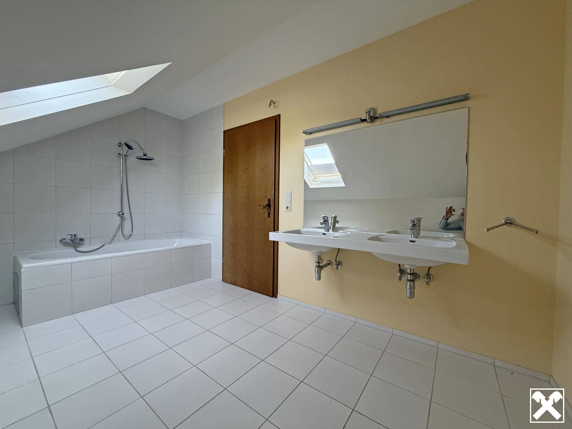 Großes Badezimmer mit Badewanne, Doppelwaschbecken und Dachfenster, das für viel Helligkeit sorgt.