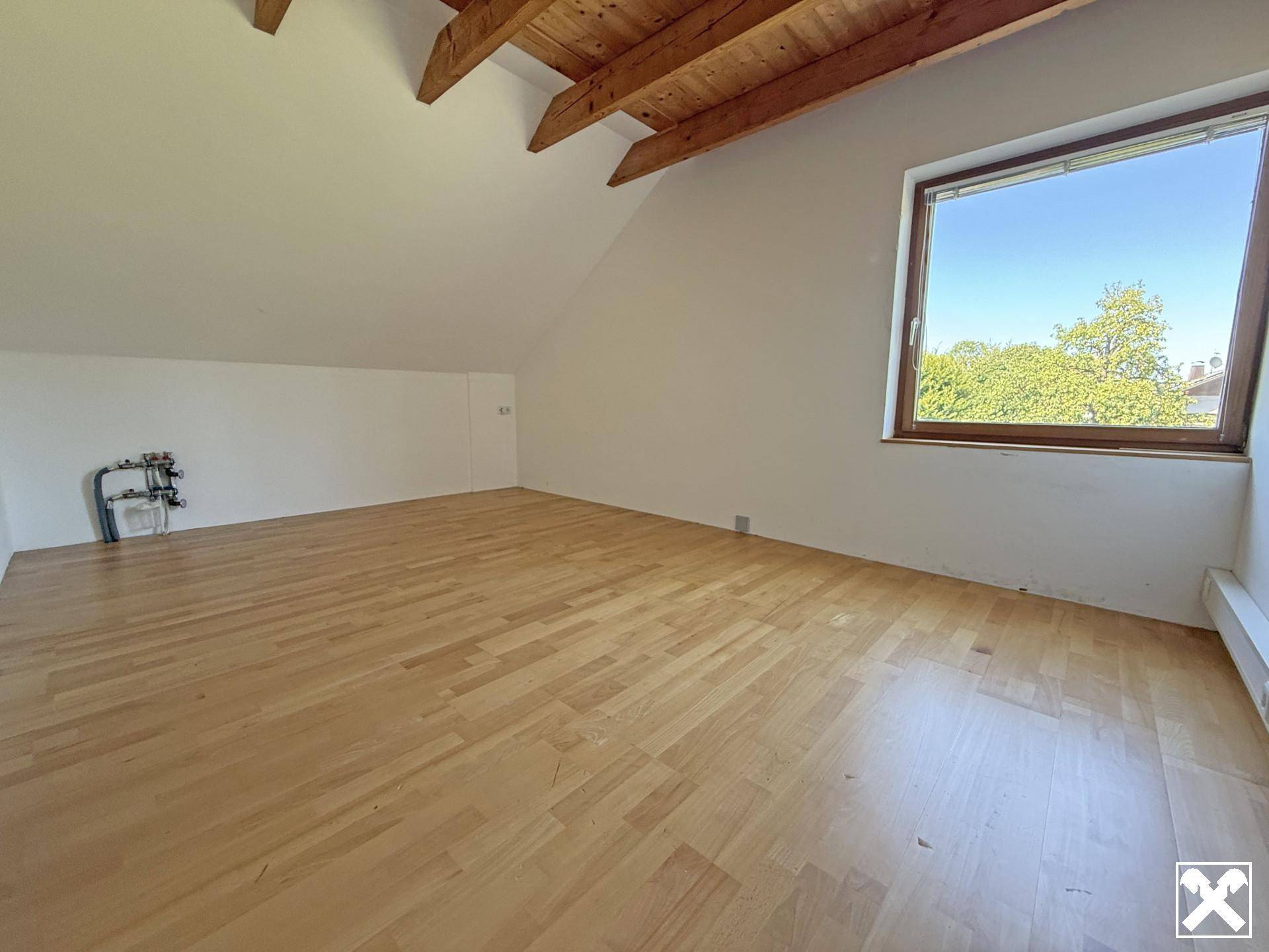 Geräumiges Schlafzimmer im Dachgeschoss mit Holzbalkendecke, Parkettboden und großem Fenster.