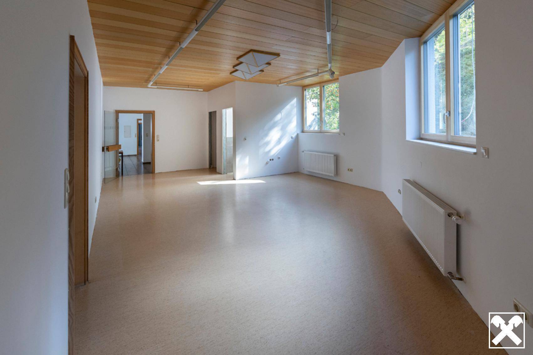 Heller, leerer Raum mit Holzdecke und großen Fenstern, ideal für Büronutzung.