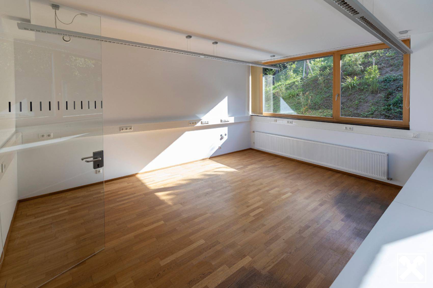 Helles Büro mit Holzboden und großen Fenstern, die viel Tageslicht hereinlassen.