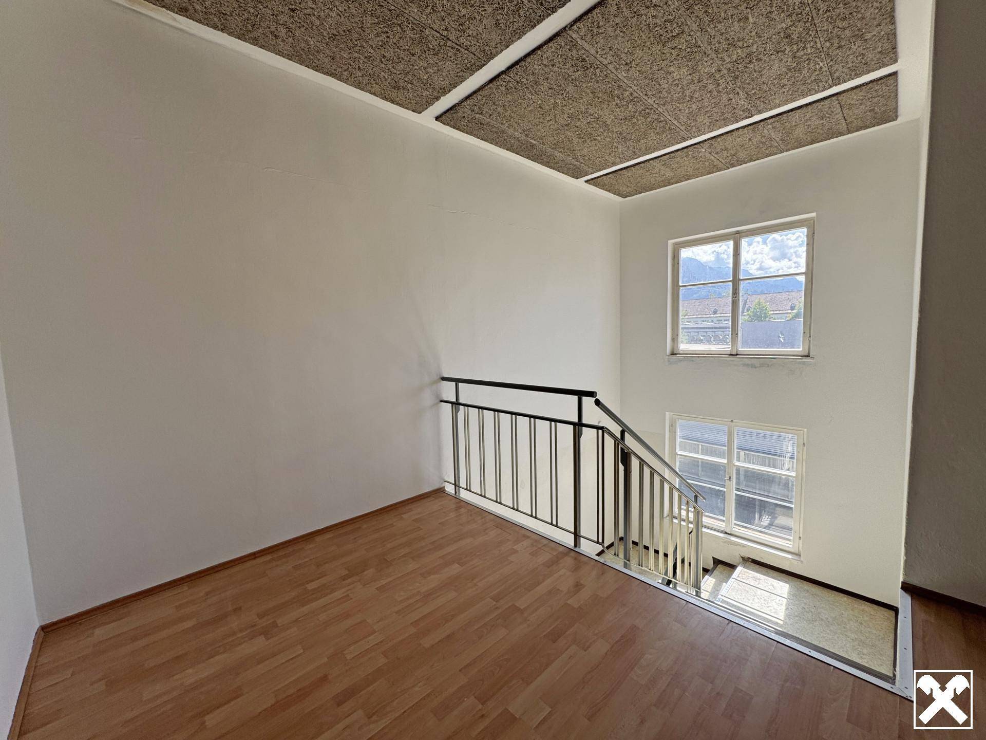 Treppenhaus mit Holzparkett auf der Etage und Blick auf die darunterliegende Treppe.