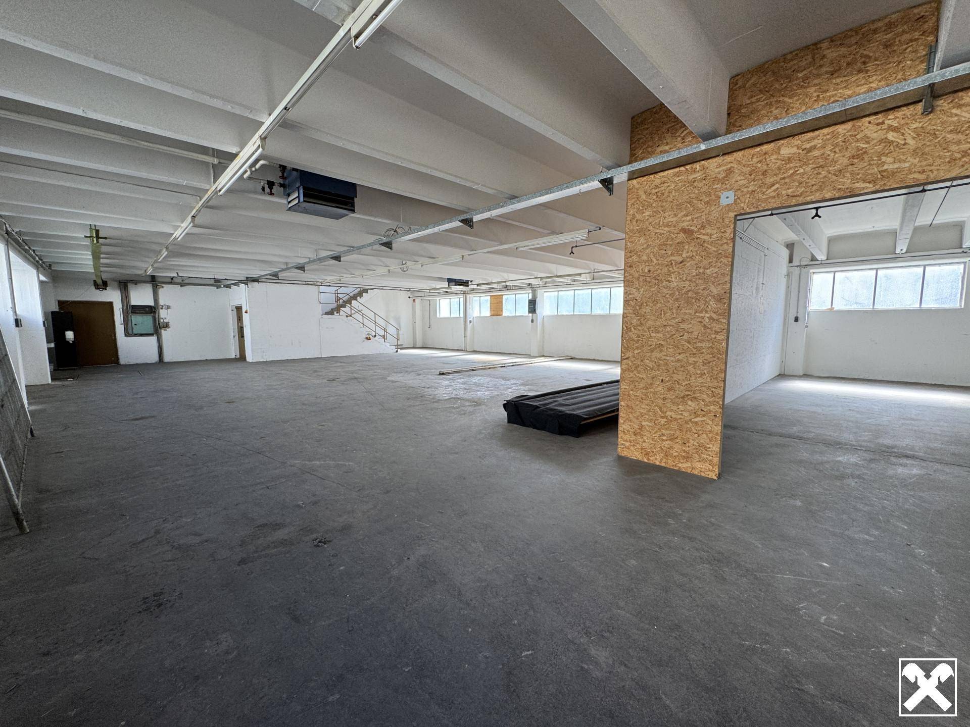Weitläufige Lagerhalle mit Betonboden, sichtbaren Trägern und einer Holzverkleidung im Hintergrund.