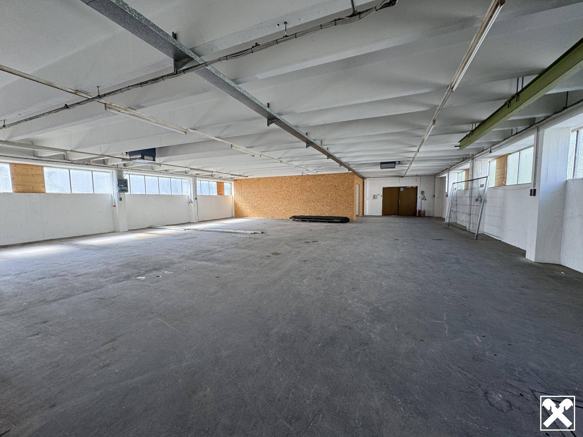 Große, offene Lagerhalle mit Betonboden, hohen Decken und vielen Fenstern für Tageslicht.