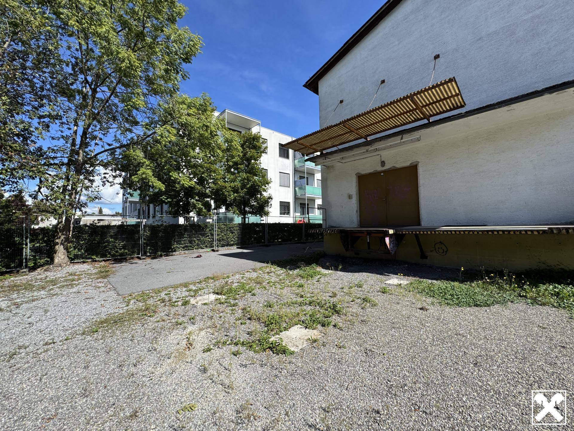 Seitenansicht eines Gebäudes mit Laderampe und einer unbefestigten Fläche daneben.