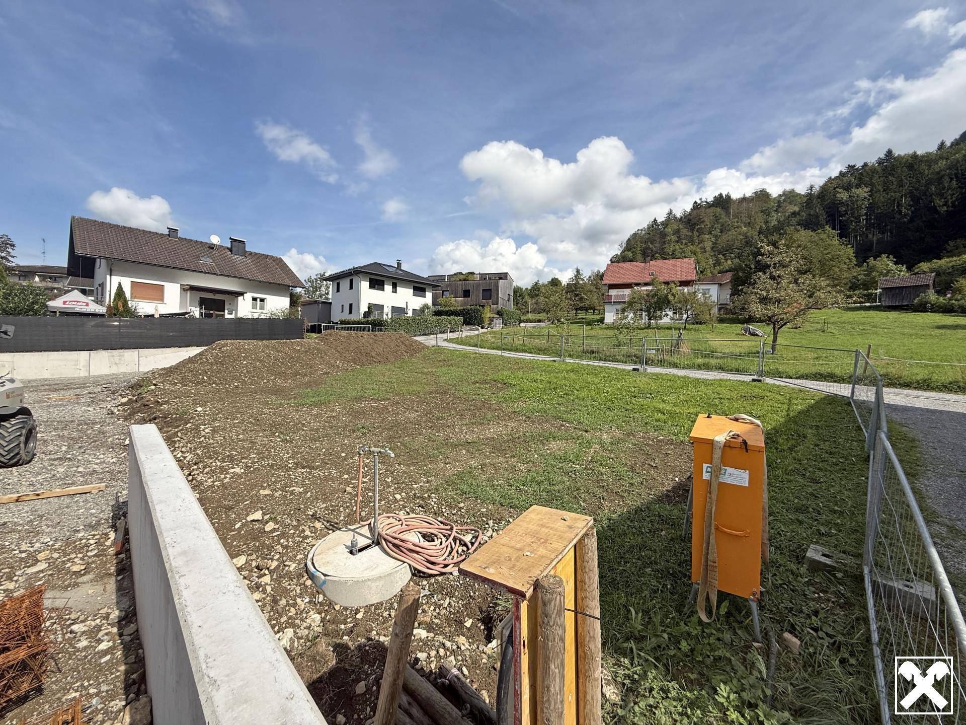 Blick über das Baugrundstück mit Erdarbeiten und weiteren Wohnhäusern in der ländlichen Umgebung.
