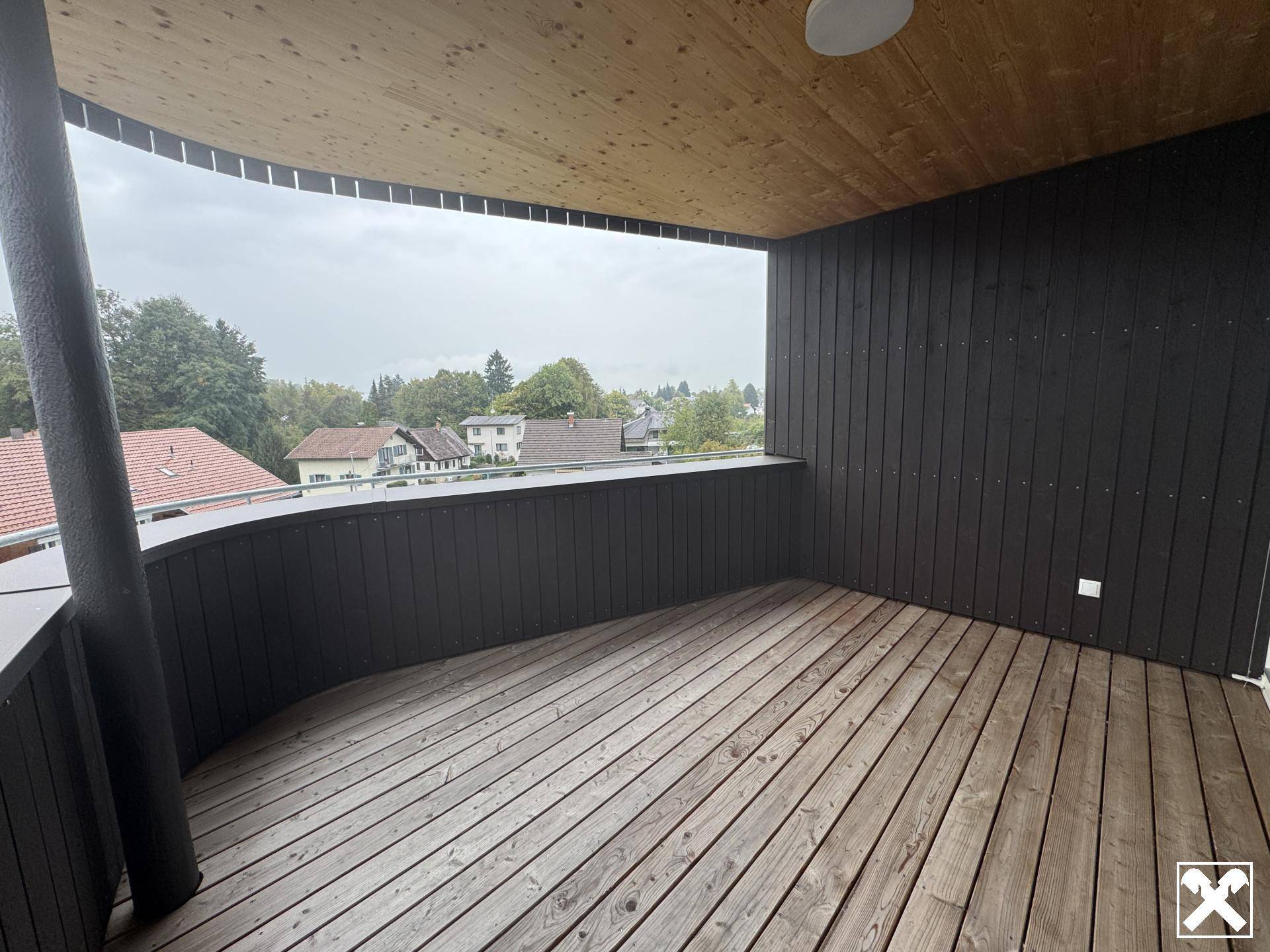 Großer Balkon mit Holzbelag und geschwungener Decke, bietet weite Ausblicke.