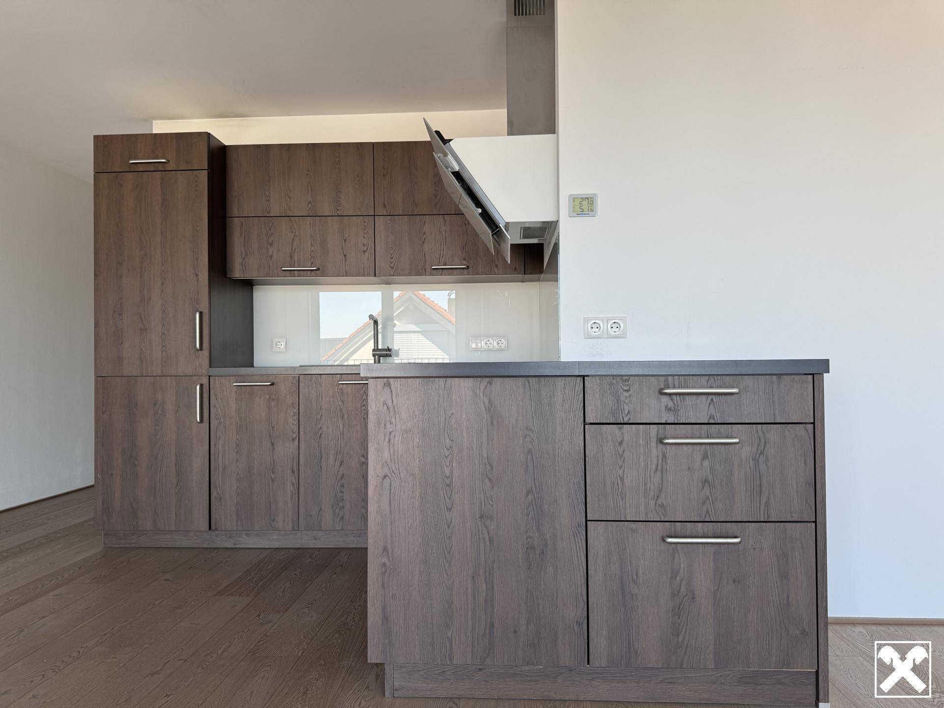 Moderne Einbauküche mit Holzoptik-Schränken, weißer Wand und Holzboden. Die Küche verfügt über eine Spüle und eine Dunstabzugshaube.