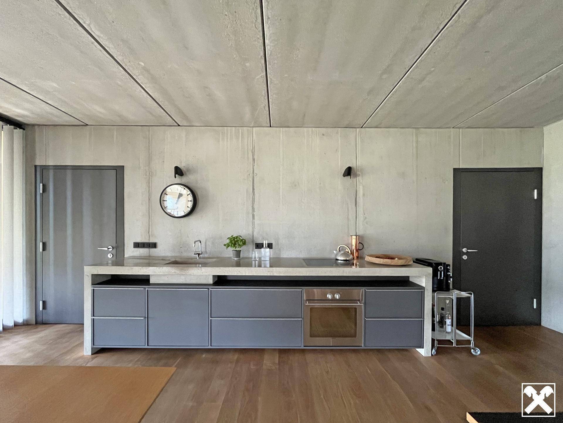 Moderne offene Küche mit grauen Fronten, Betonwänden und Holzboden in minimalistischem Design.