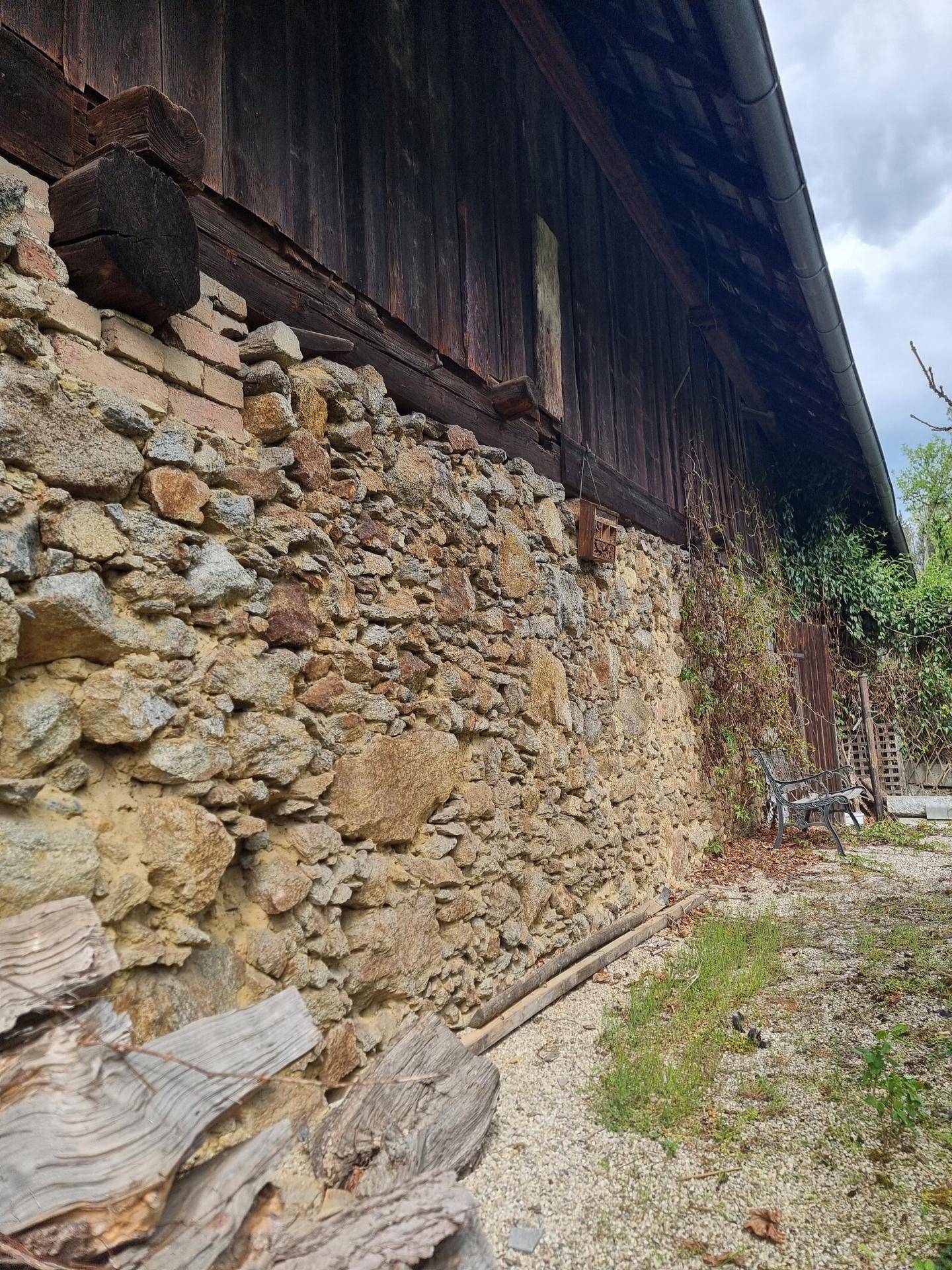 Rustikale Steinmauer eines alten Gebäudes mit Holzelementen und Bewuchs.