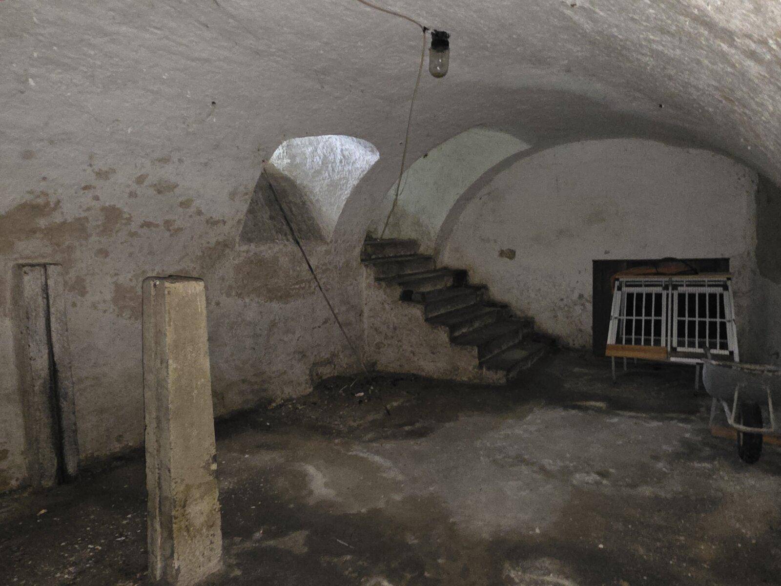 Dunkler Gewölbekeller mit rauen Wänden und einer Treppe, die in den Raum führt.