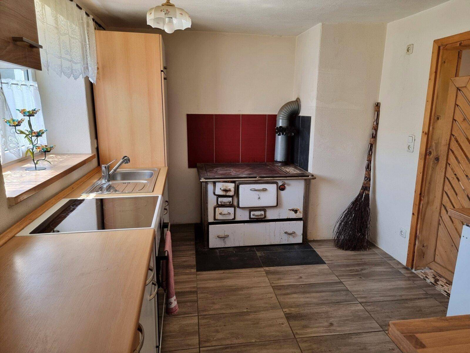 Traditionelle Küche mit einem alten Holzofen, einfachen Holzschränken und Fliesenboden.