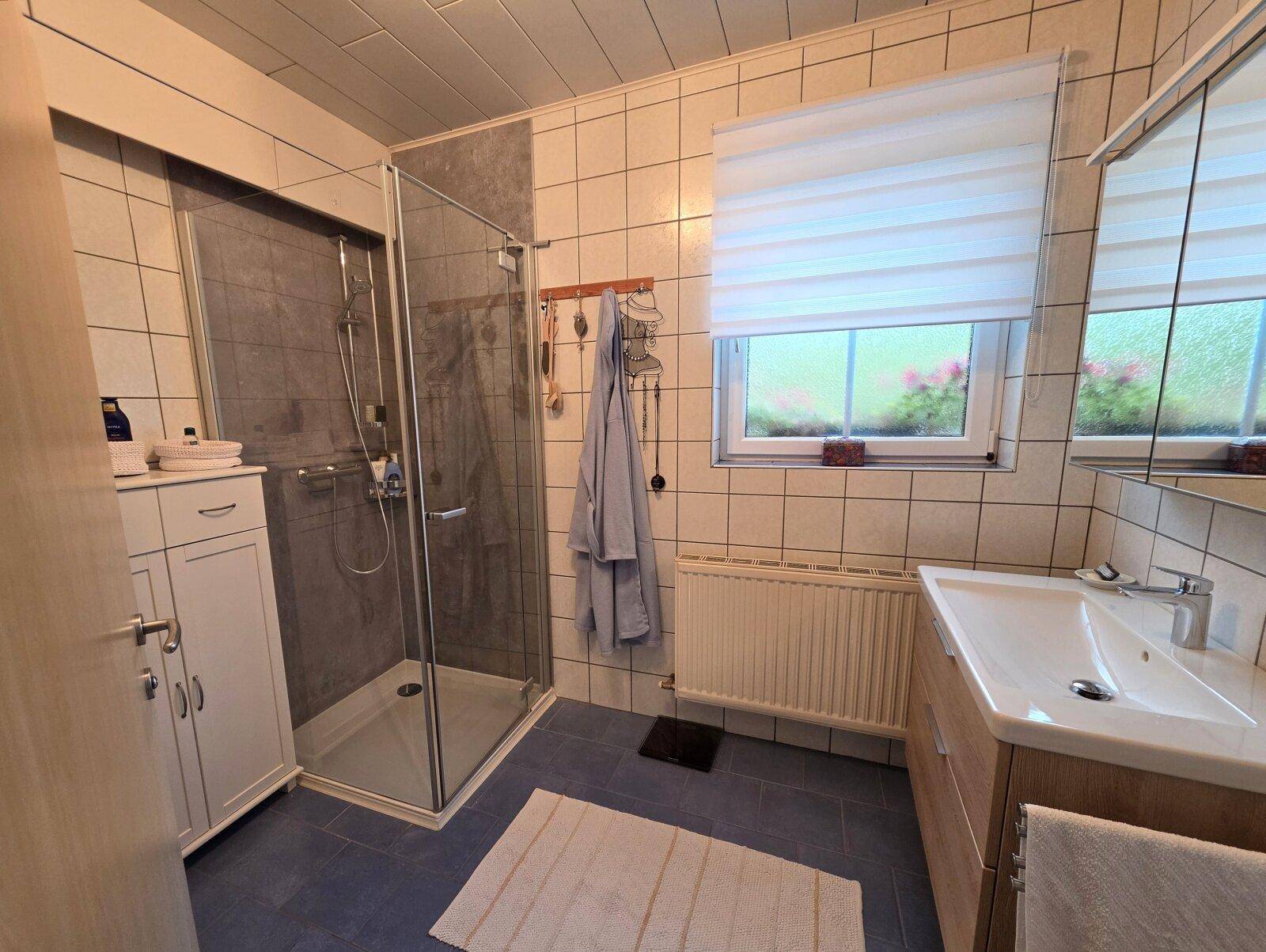 Modernes Badezimmer mit ebenerdiger Dusche, Waschbecken und Fenster für Tageslicht.