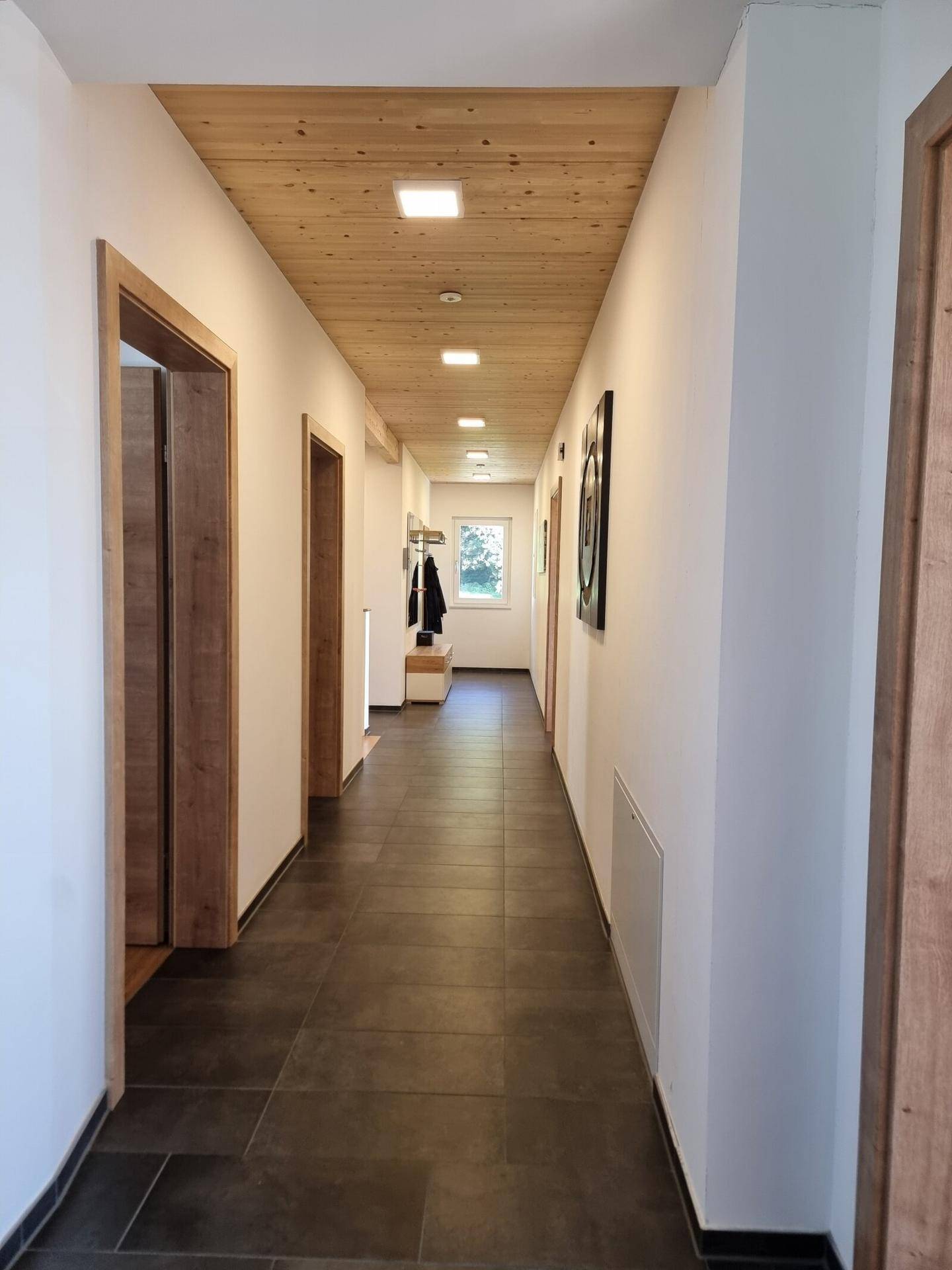 Langer Flur mit Holzdecke, dunklen Fliesen und modernen Holztüren.