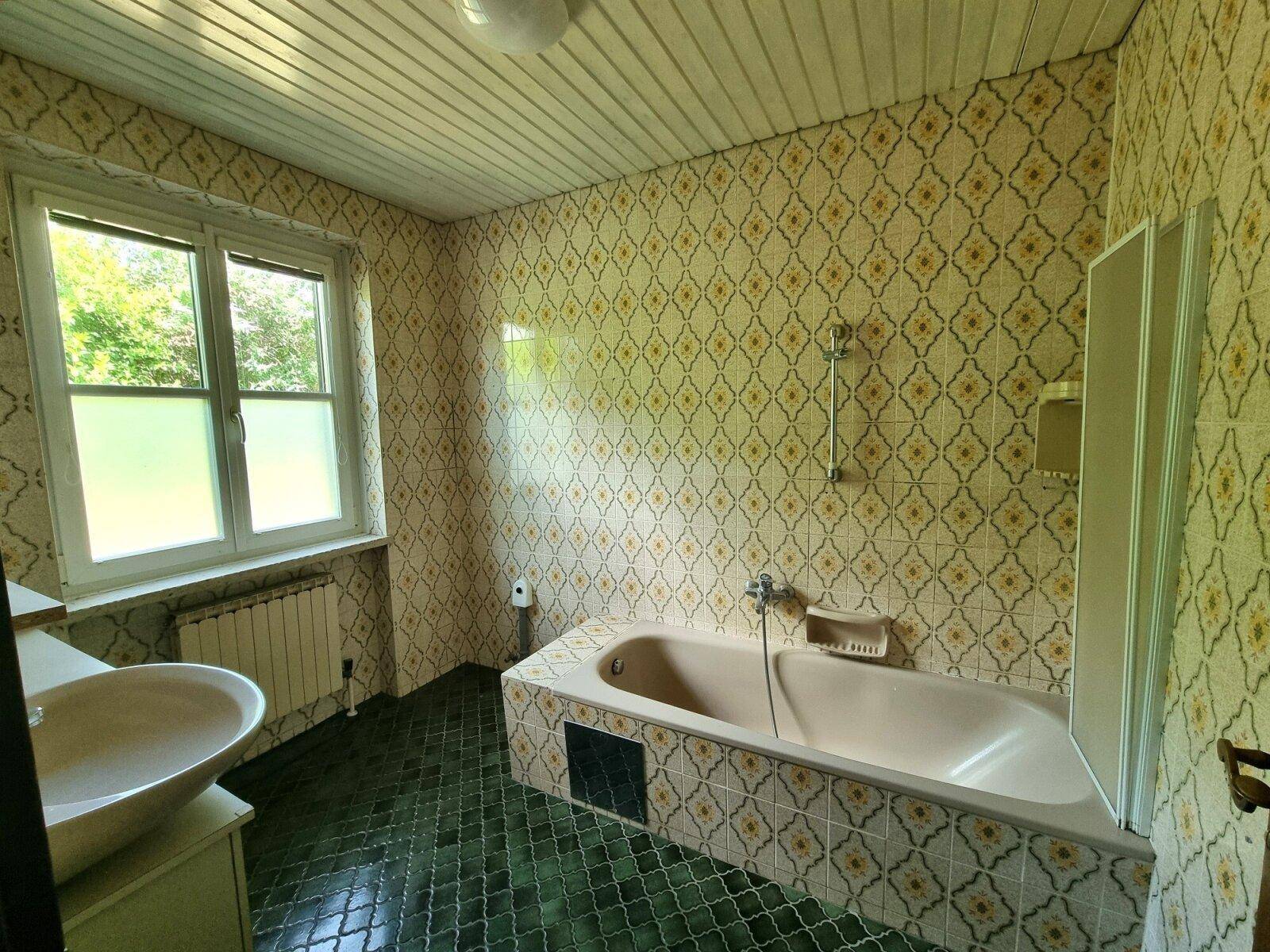 Badezimmer im 80er-Jahre-Stil mit gemusterten Fliesen, Badewanne und Fenster.