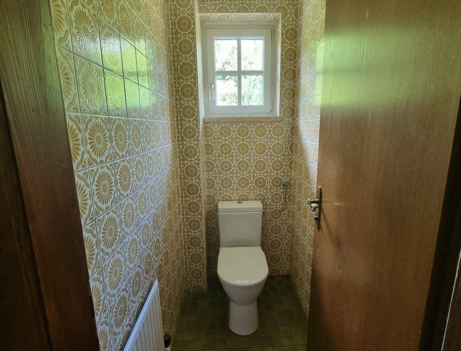 Separate Toilette mit Fenster und gemusterten Fliesen im Stil der 80er Jahre.