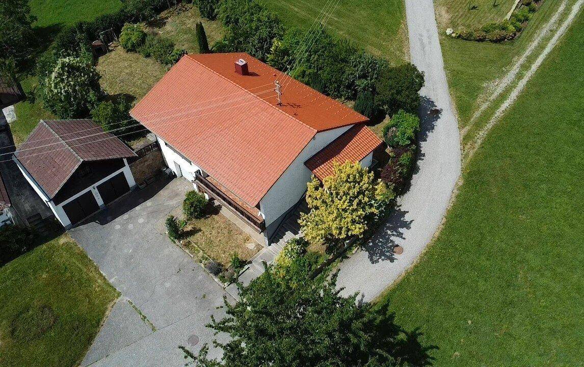 Luftaufnahme eines Einfamilienhauses mit rotem Ziegeldach, umgeben von grünen Wiesen und Bäumen.