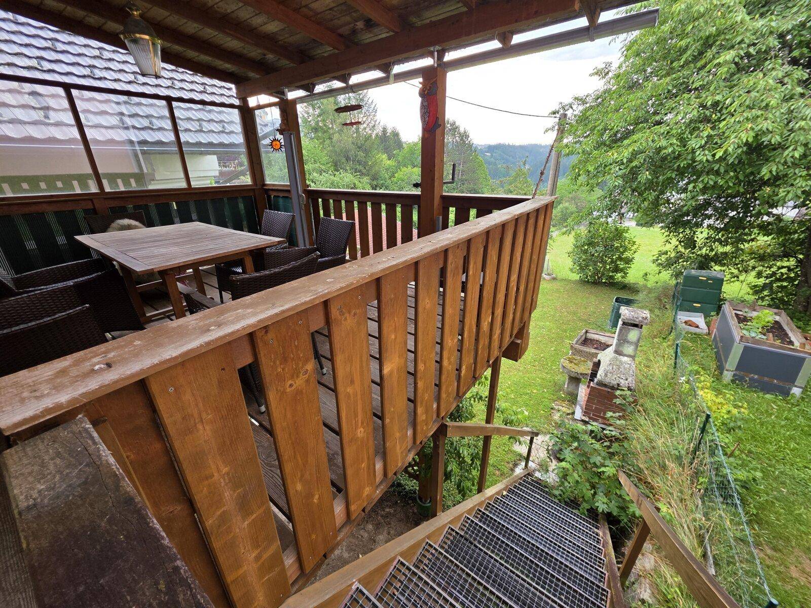 Blick von der überdachten Terrasse hinunter in den Garten und die umliegende grüne Landschaft.