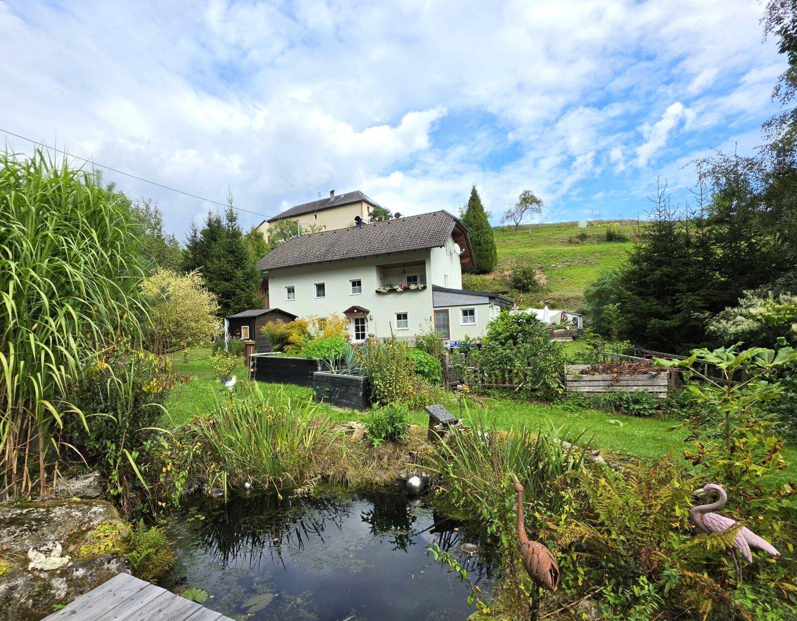 Idyllischer Gartenbereich mit Teich und üppiger Vegetation, umgeben von grünen Hügeln.