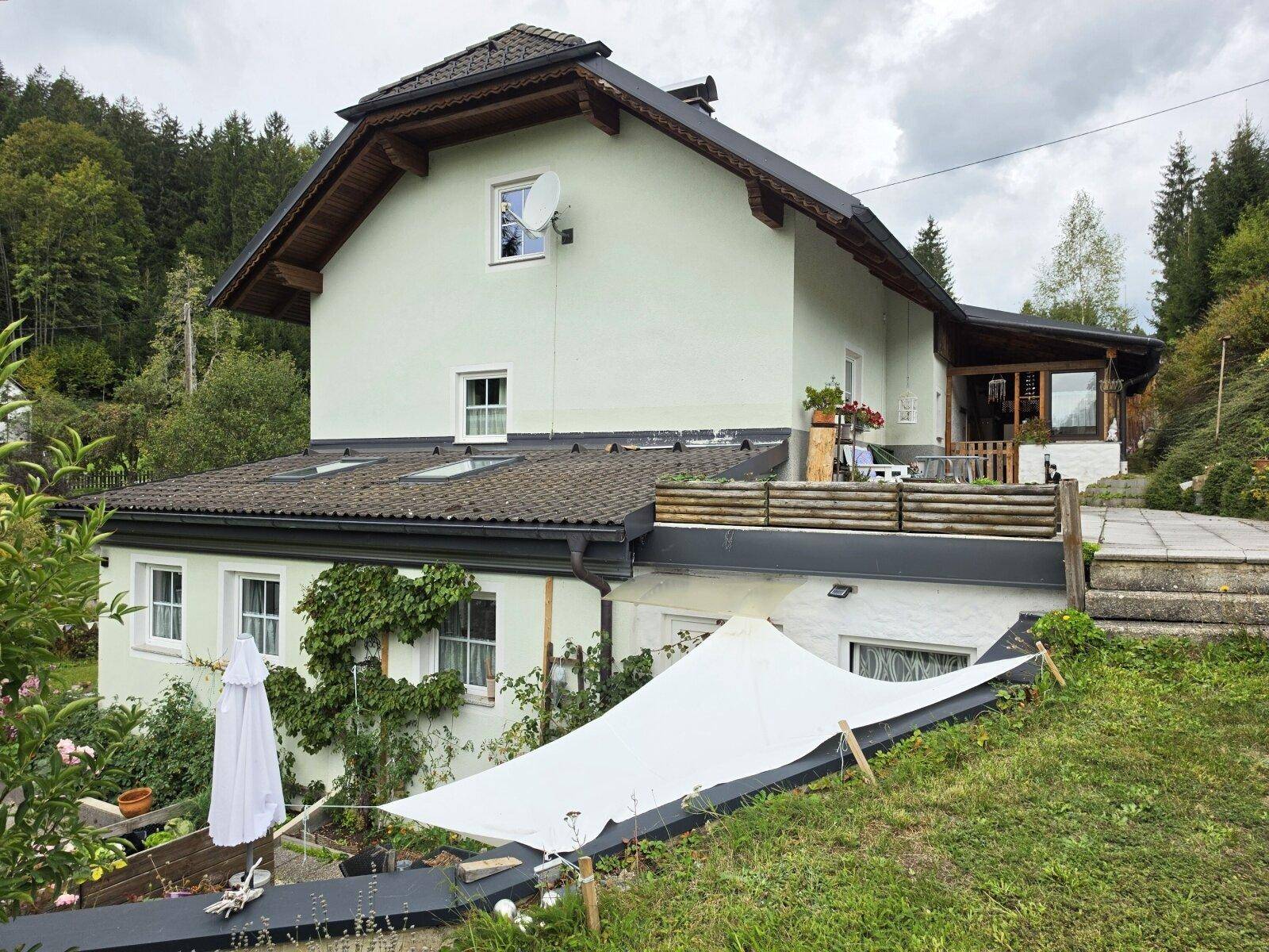 Rückseite des Hauses mit Terrasse und Sonnensegel, umgeben von grüner Landschaft.