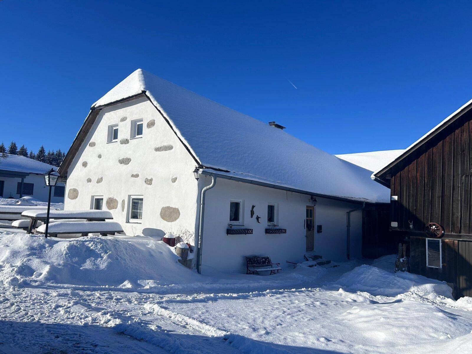 Das Haus im Winter, vollständig mit Schnee bedeckt unter einem klaren blauen Himmel.