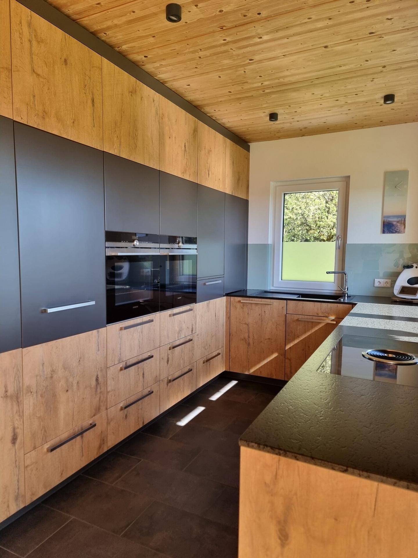 Moderne Einbauküche mit Holz- und Anthrazitfronten, dunkler Arbeitsplatte und Fenster.