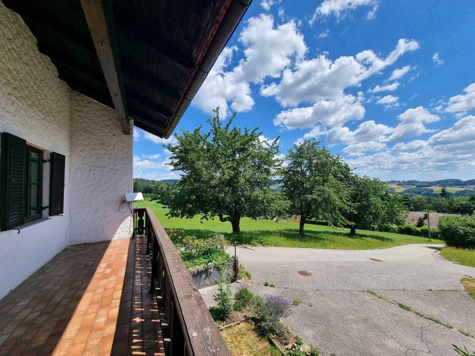 Balkon mit Holzbalkongeländer und weitem Blick über grüne Felder und die ländliche Umgebung.