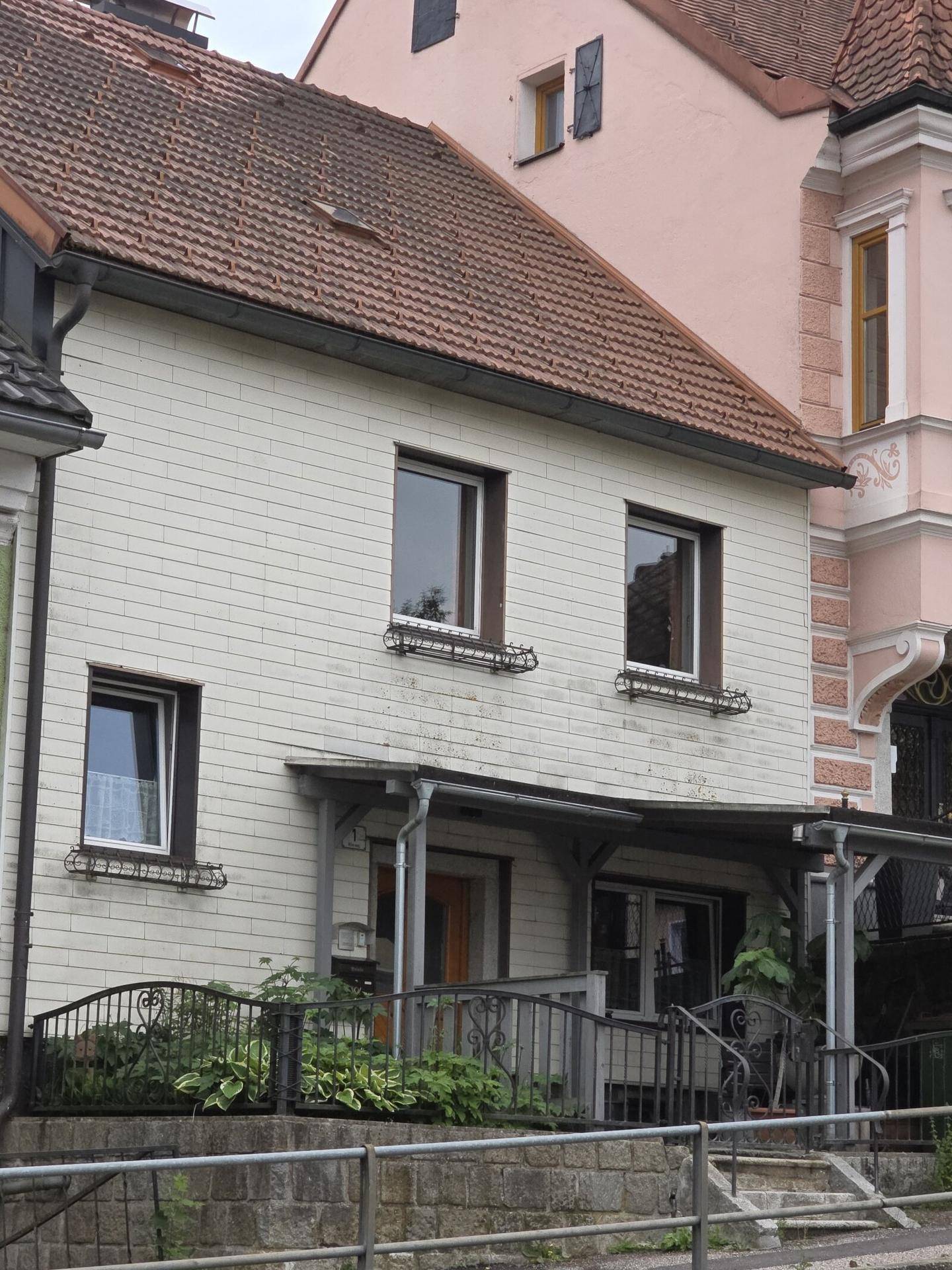 Vorderansicht des Hauses mit weißer Fassade, braunen Fenstern und einem überdachten Eingangsbereich.