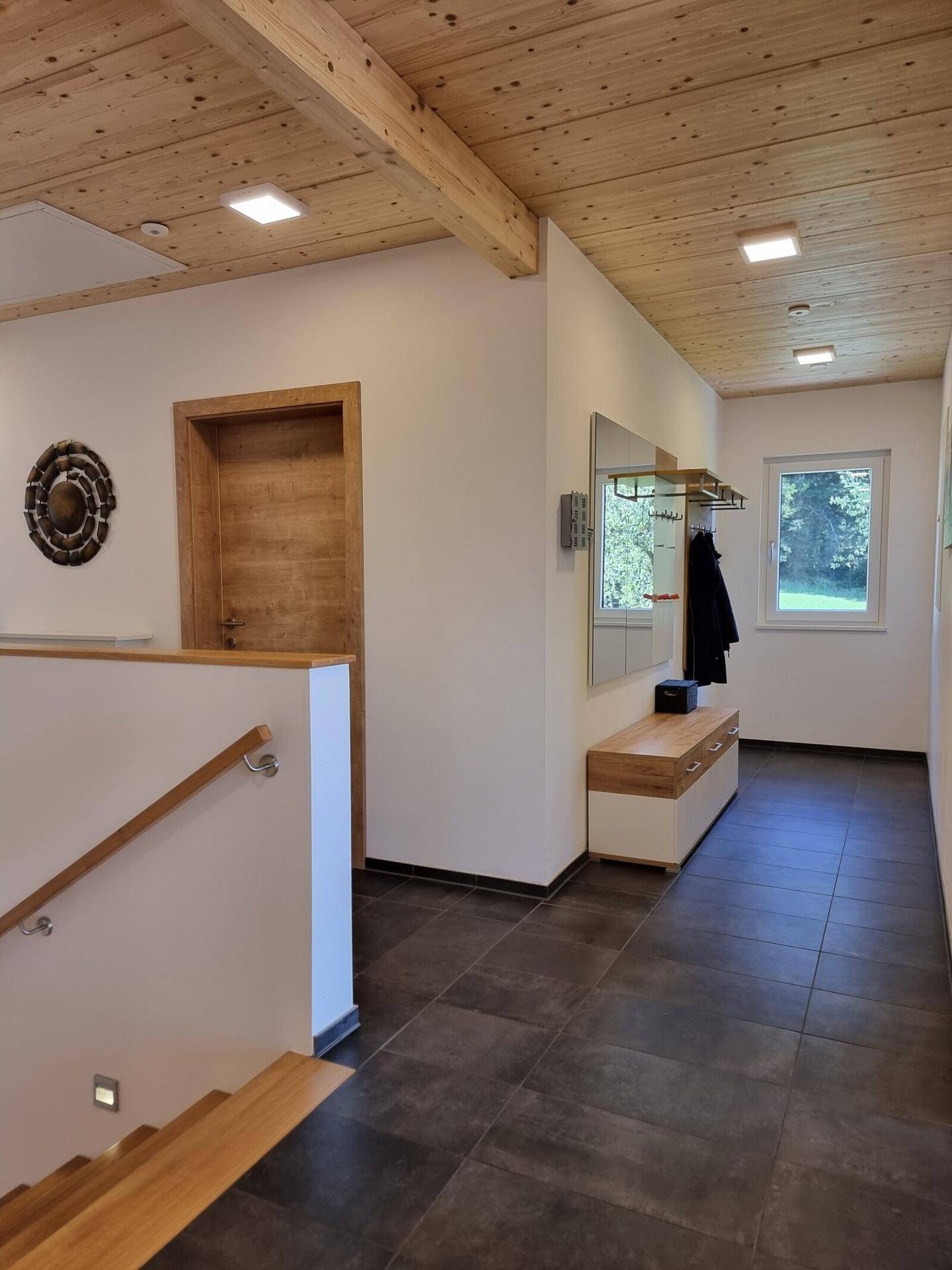 Heller Eingangsbereich mit Holzdecke, Fliesenboden und Treppe zum Obergeschoss.