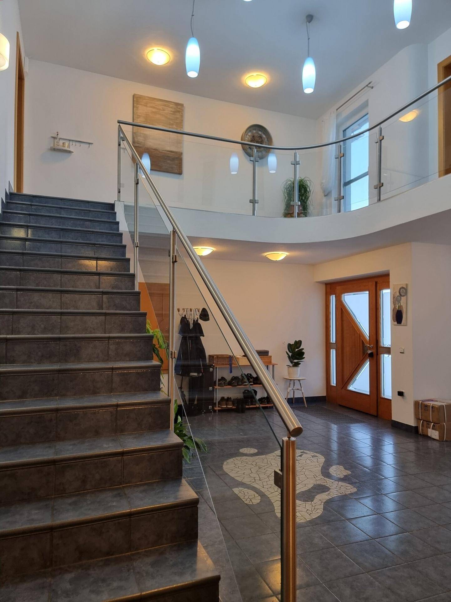 Heller Eingangsbereich mit Treppe, Glasgeländer und dekorativem Bodenmuster.