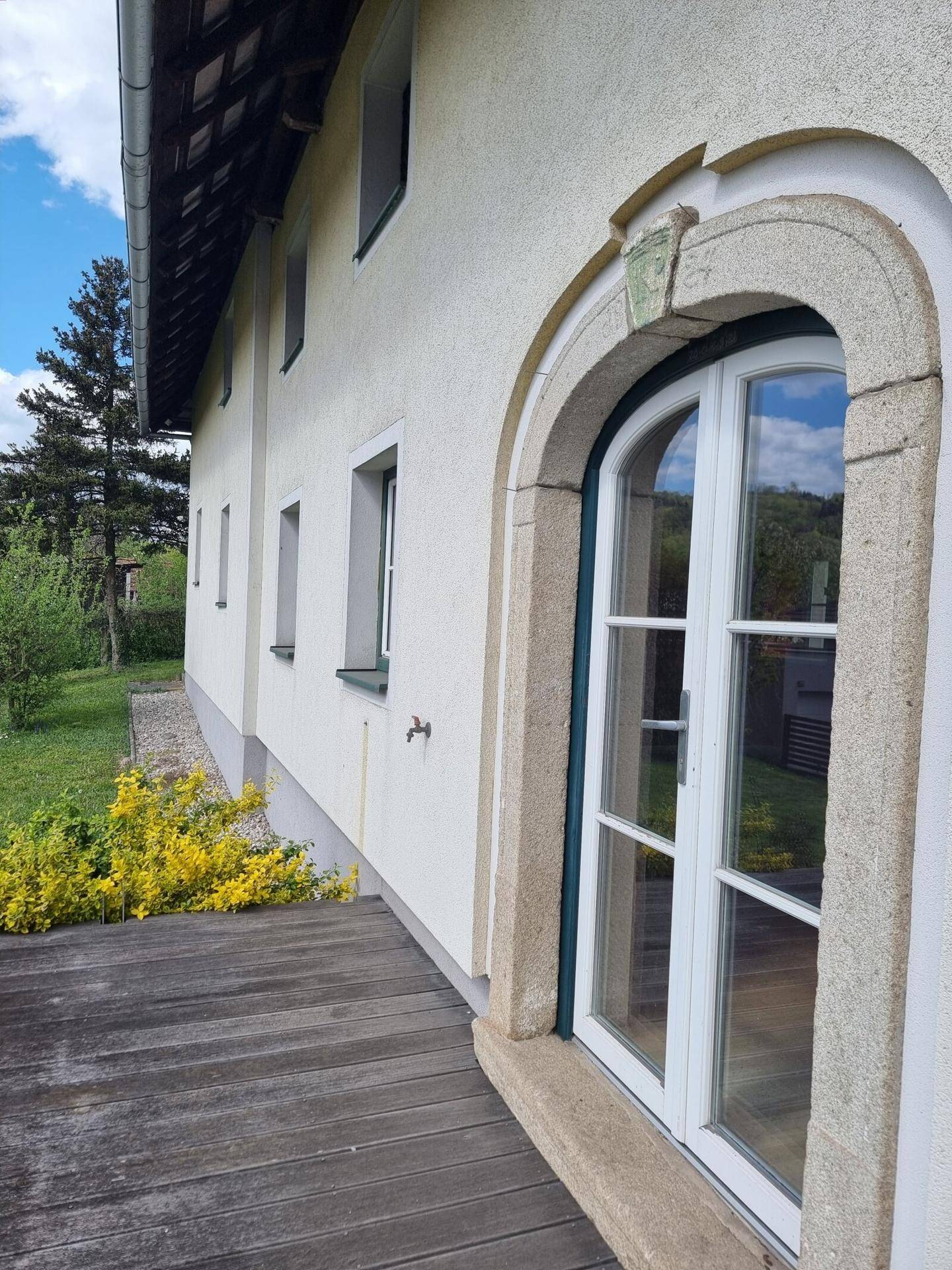 Holzterrasse entlang der Hausfassade mit Blick auf die grüne Umgebung.