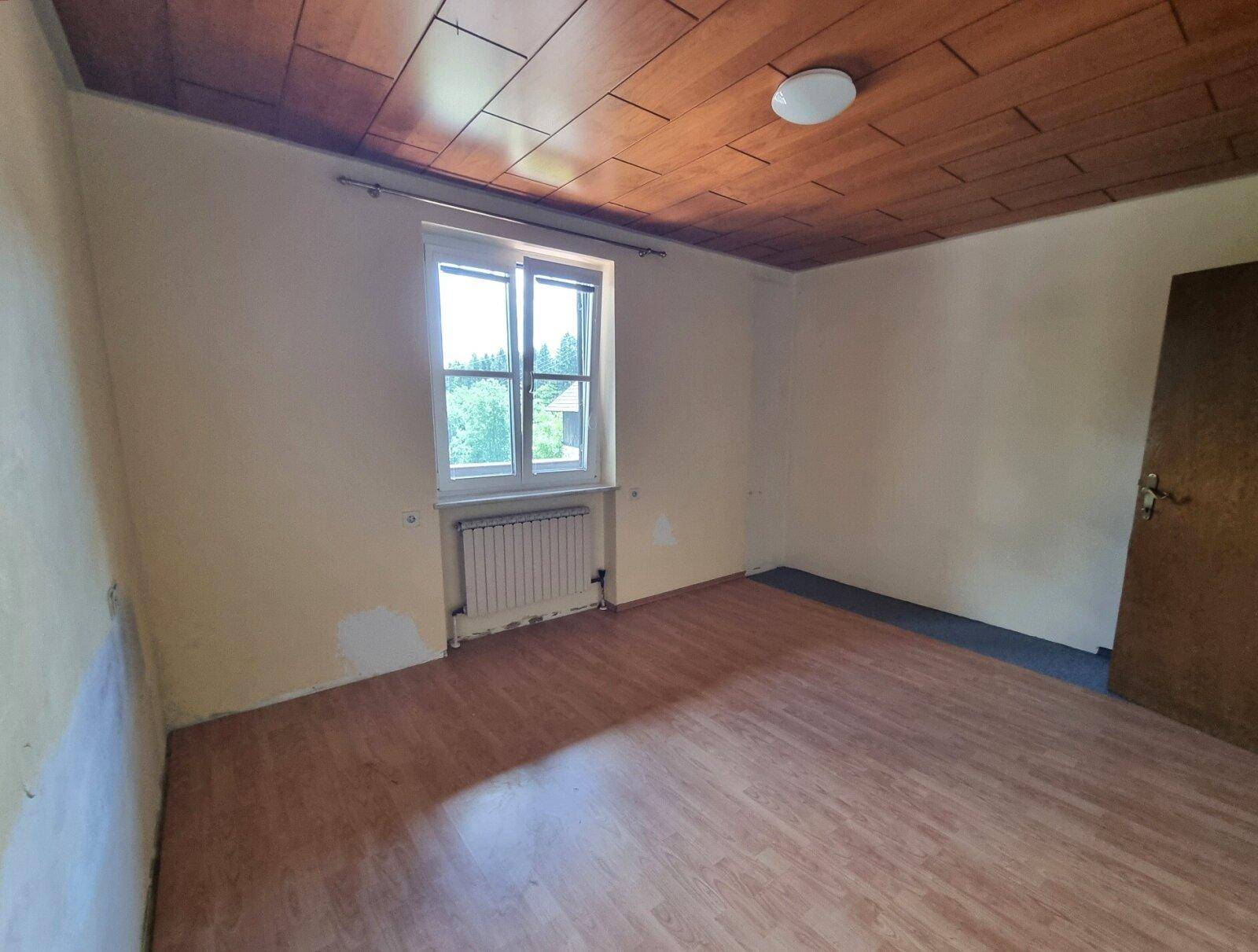 Schlafzimmer mit Holzbalkendecke, Laminatboden und Fenster mit Blick ins Grüne.